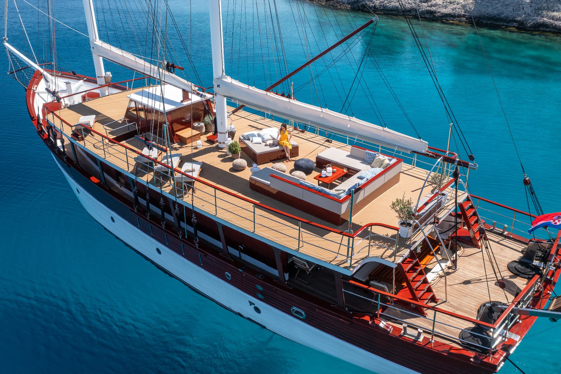 Large wooden sailboat anchored in bright turquoise coastal waters near rocky shore