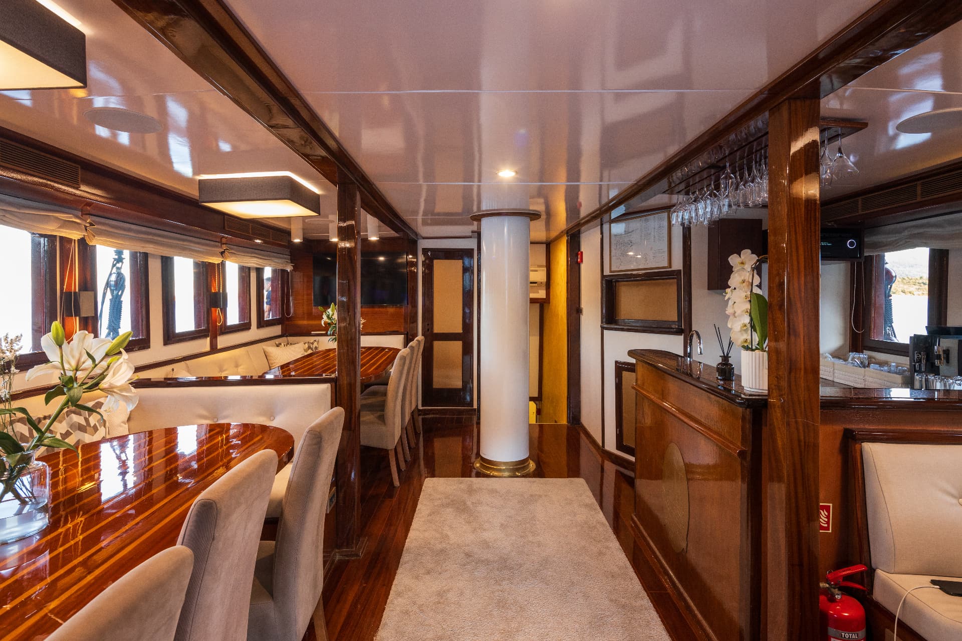 Interior dining area and bar of a yacht with polished wood, white seating, and flowers.