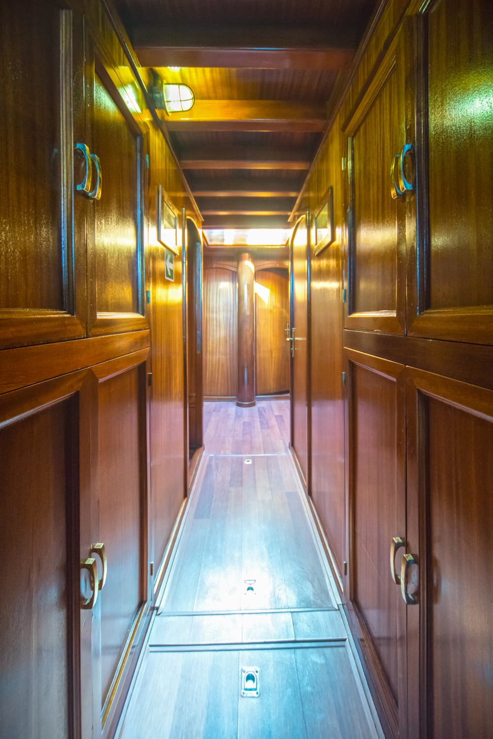 Narrow wooden hallway interior with polished cabinetry and bright central floor lighting.