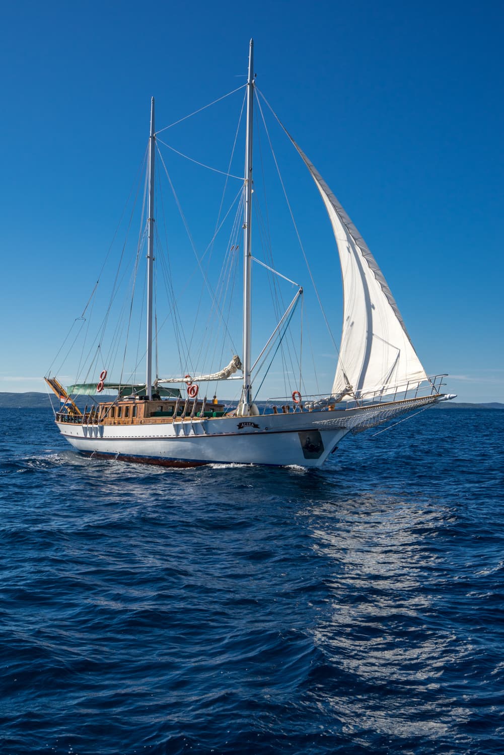 White sailing yacht named Alisa on deep blue, choppy water under clear sky.