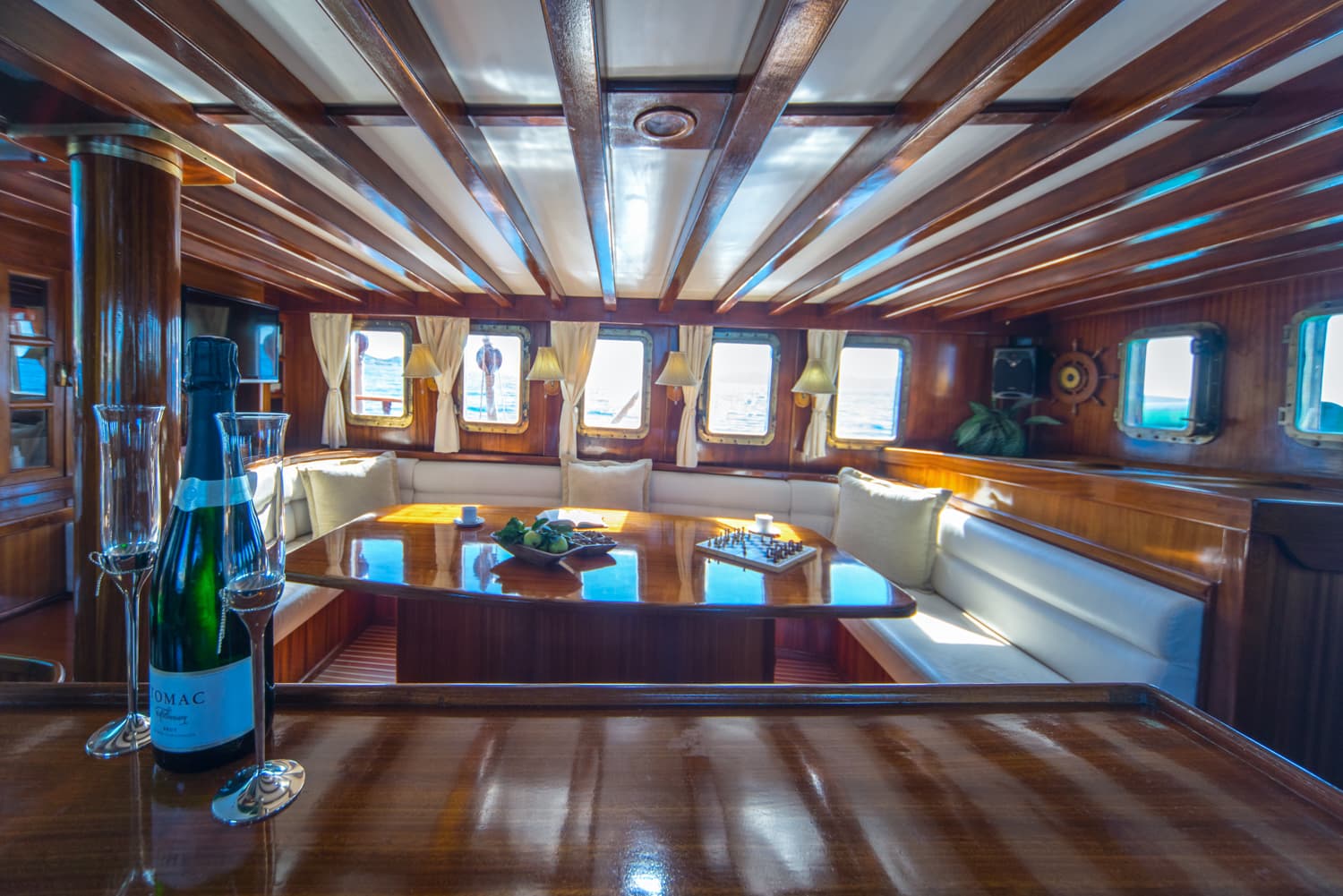 Champagne bottle and glasses inside a yacht cabin with wooden paneling and sea views.