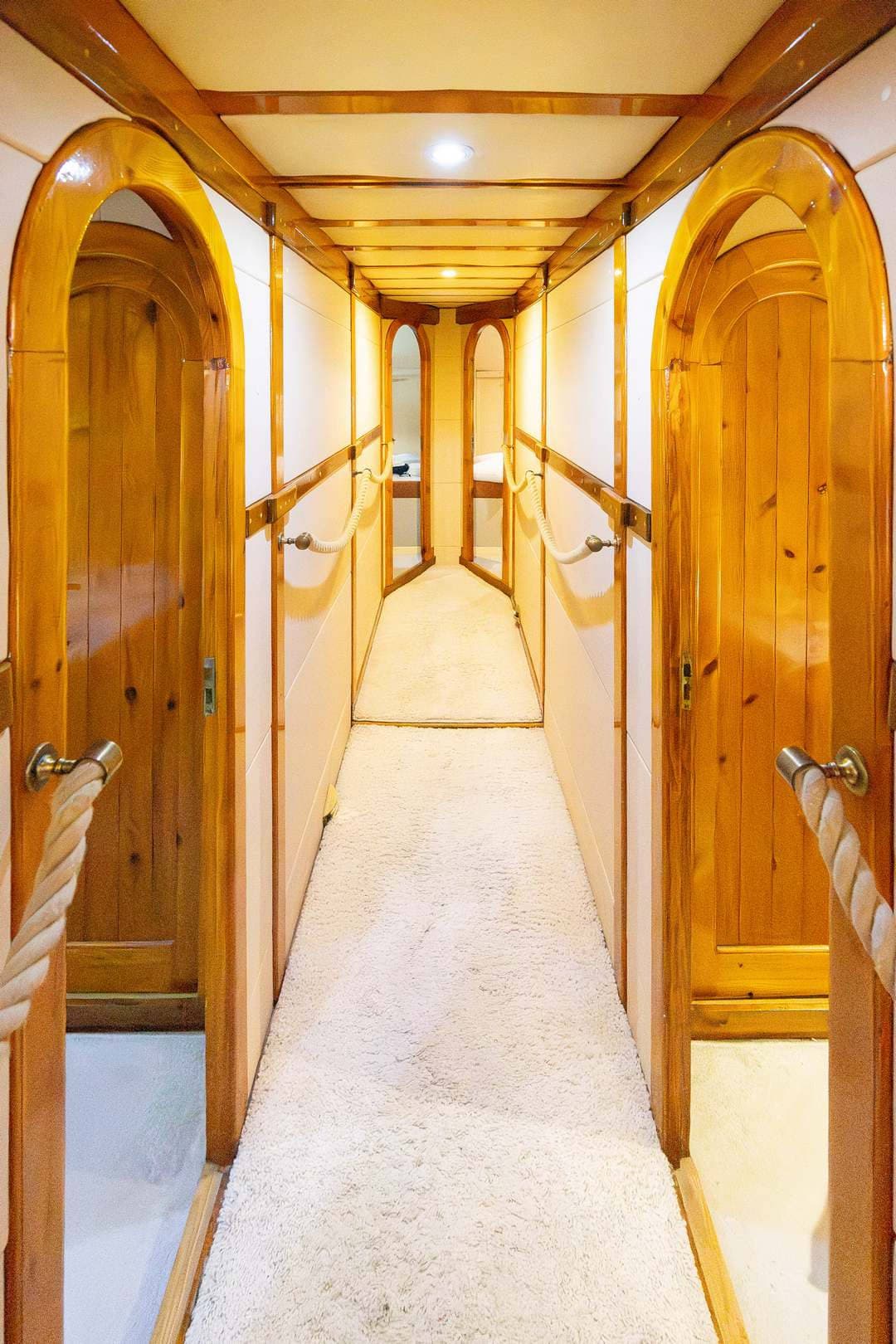 Narrow interior hallway with wood trim, arched doorways, and rope handrails, likely on a boat.