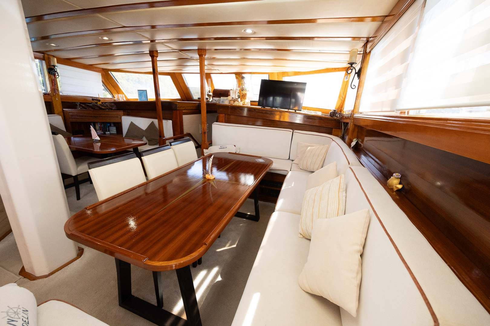 Interior salon of a yacht with glossy wood trim, white seating, and a large dining table.