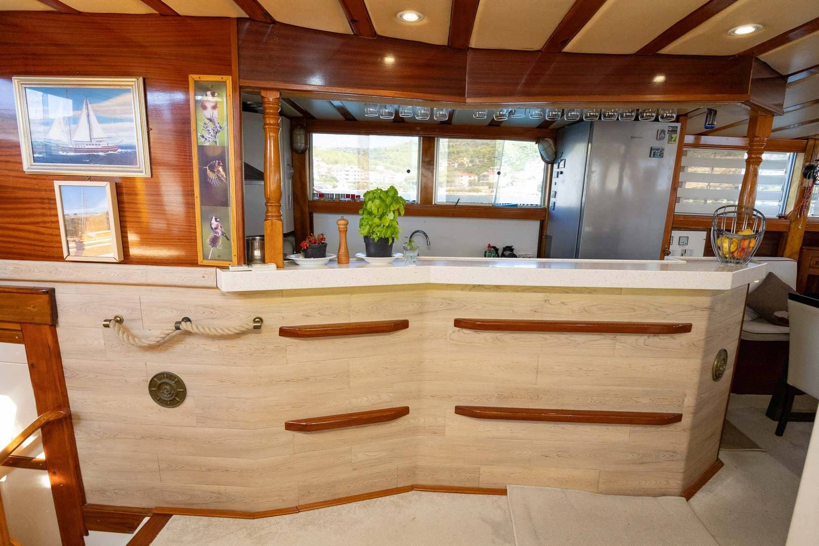 Interior bar area of a boat with wood paneling, rope detail, and view of coastal buildings.
