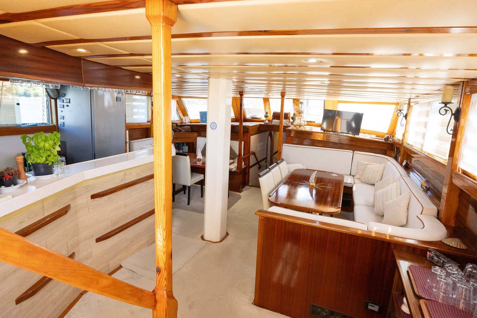 Interior cabin of a yacht with wood trim, white seating, dining table, and kitchen area.