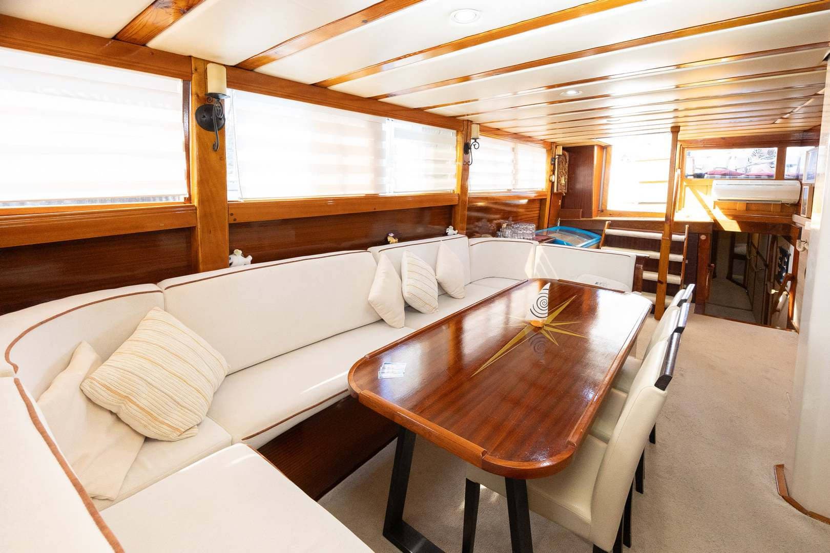 Boat interior dining area with white upholstery, wood trim, and a compass rose inlay table.