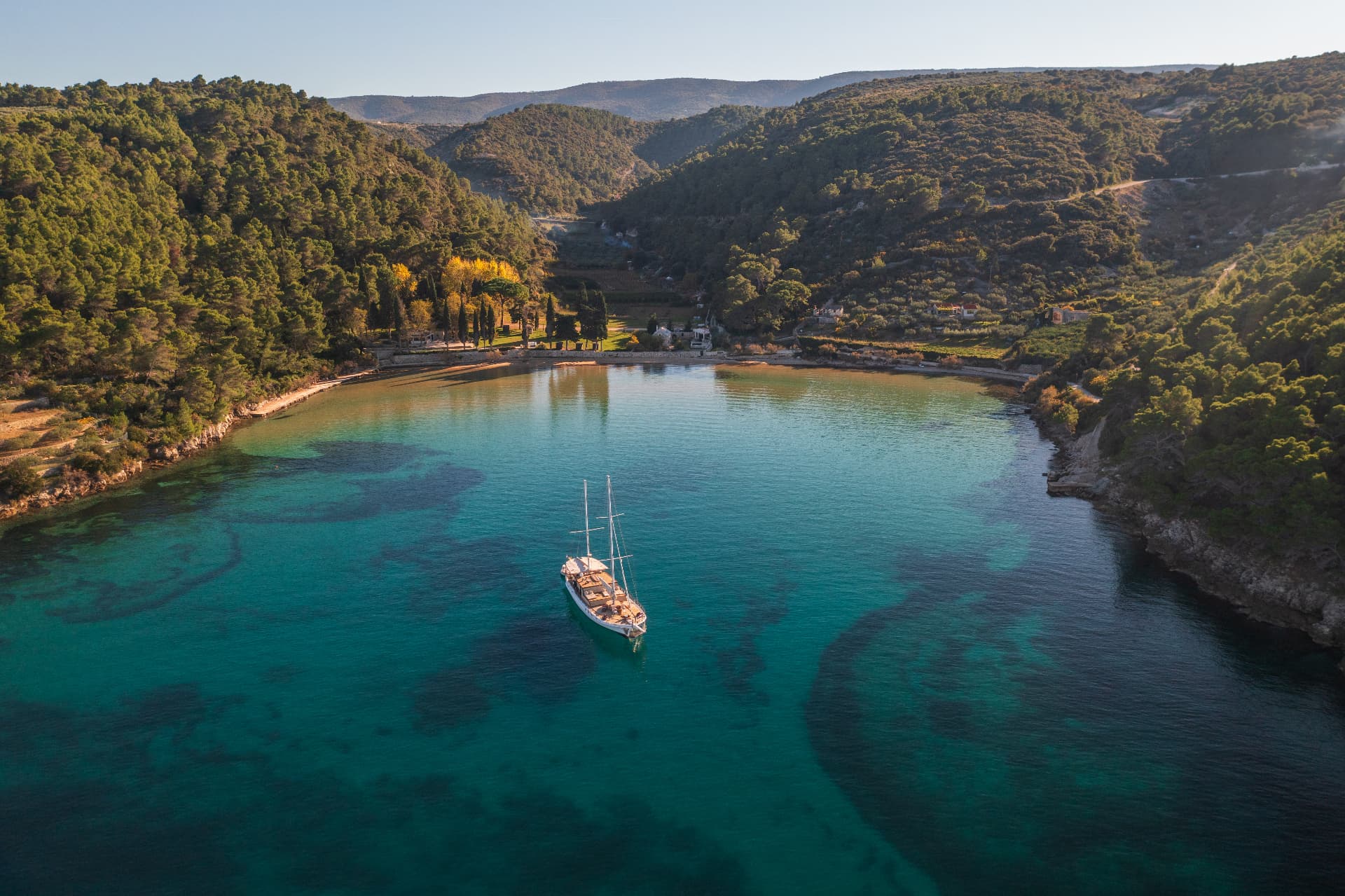 Sailboat anchored in turquoise cove surrounded by densely forested hillsides.