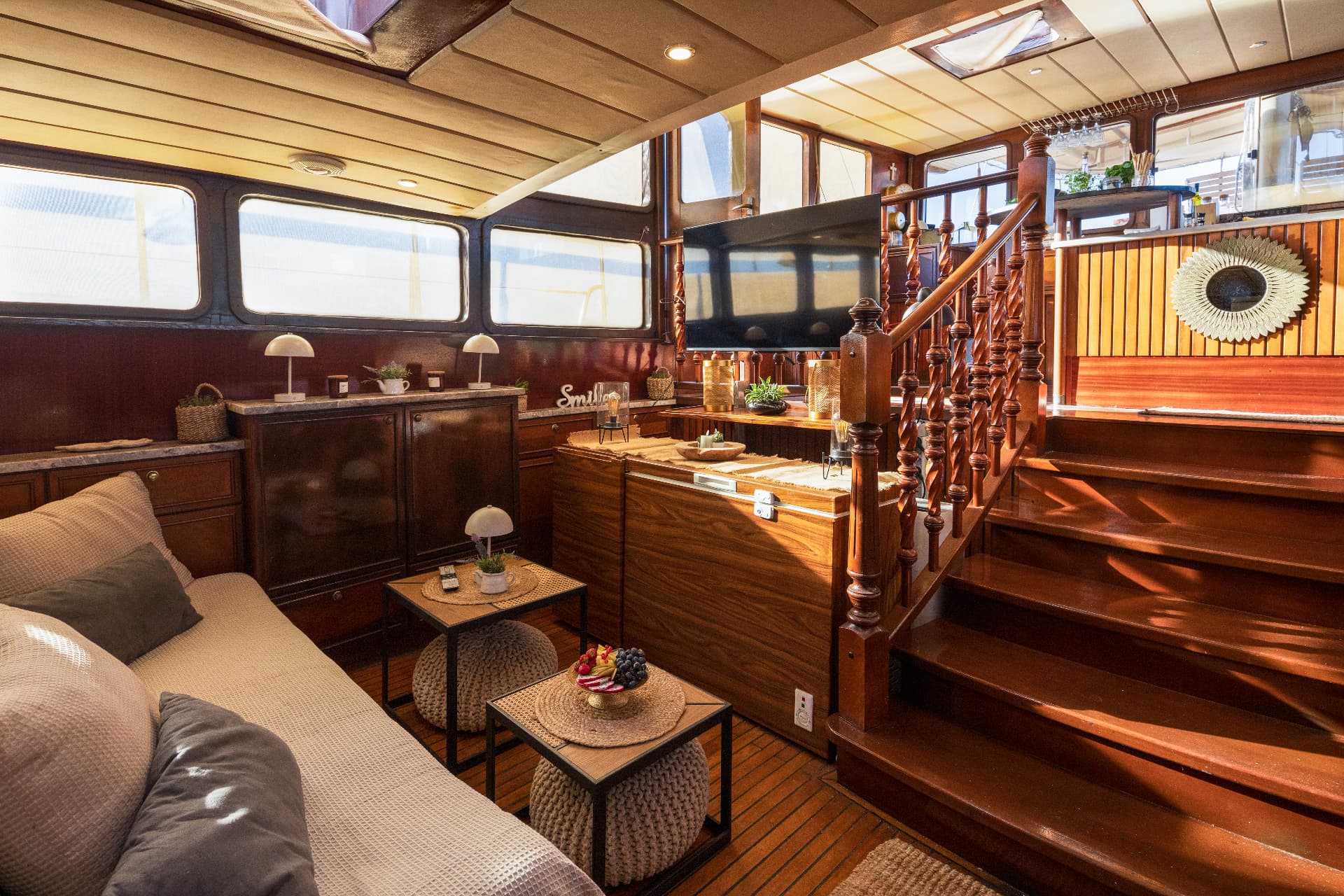 Interior cabin lounge with wood paneling, sofa, and dark wooden staircase on a boat.
