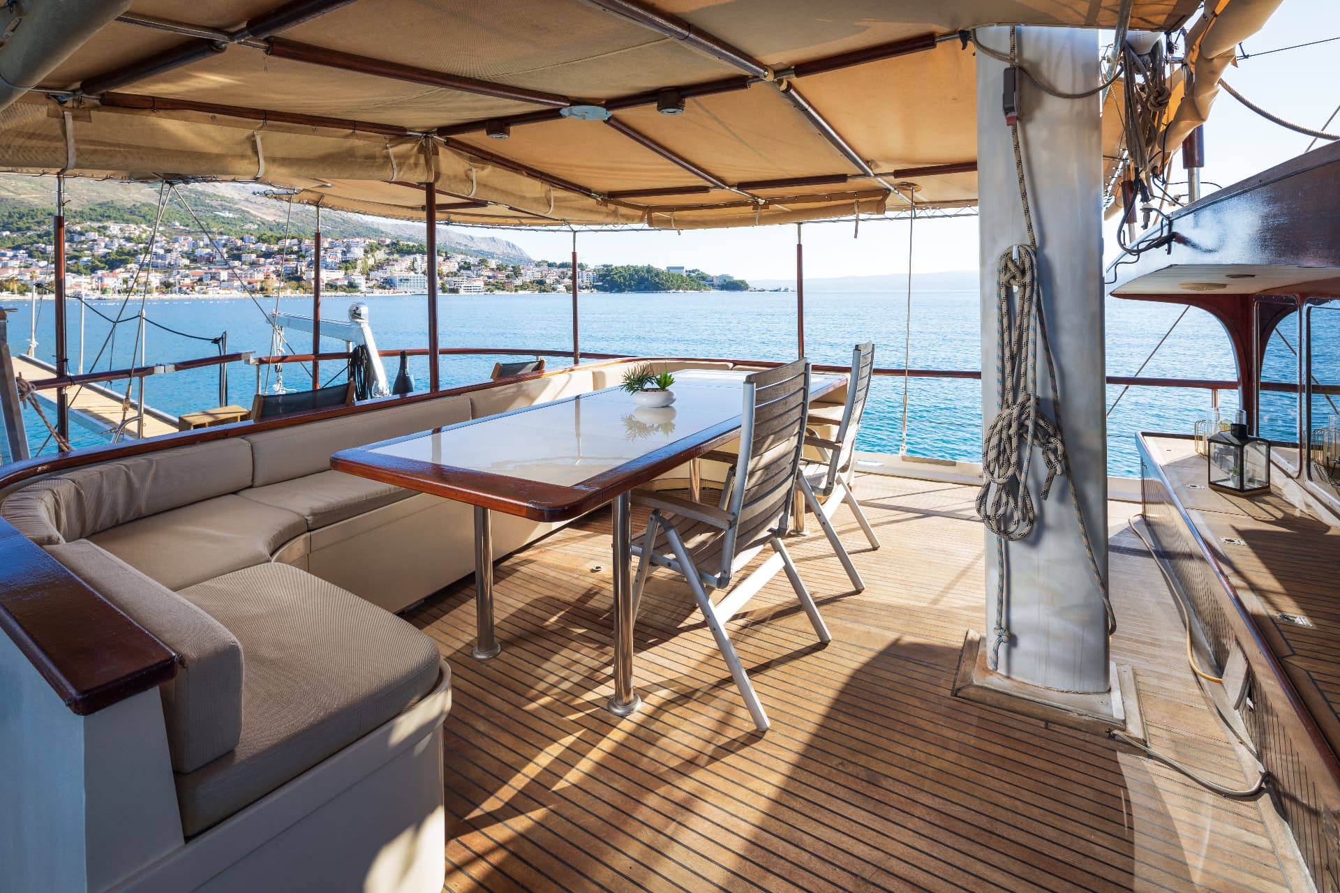 Boat deck dining area with teak flooring overlooking coastal town and blue sea
