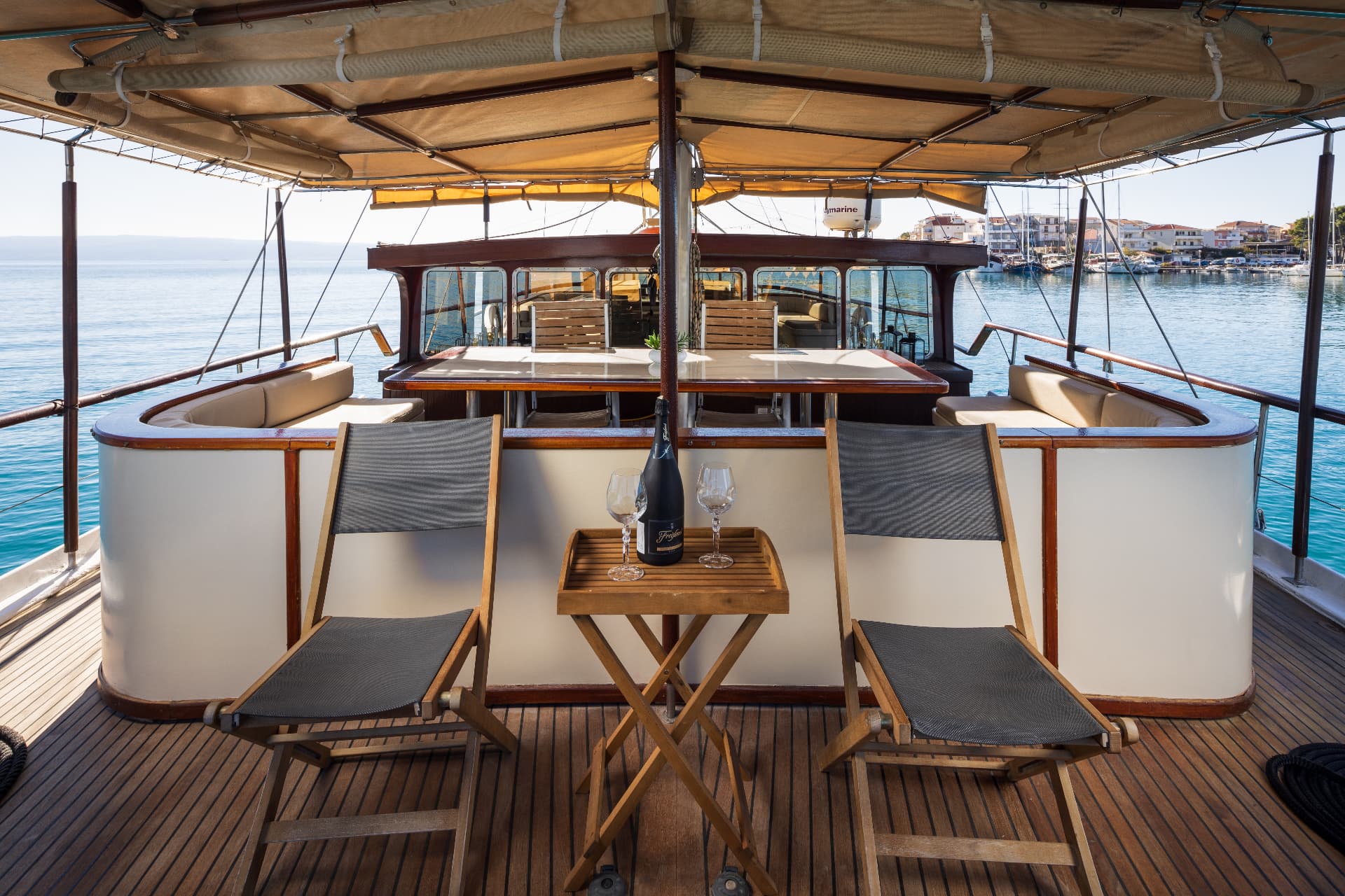 Deck seating with champagne and glasses on a boat near a coastal town harbor