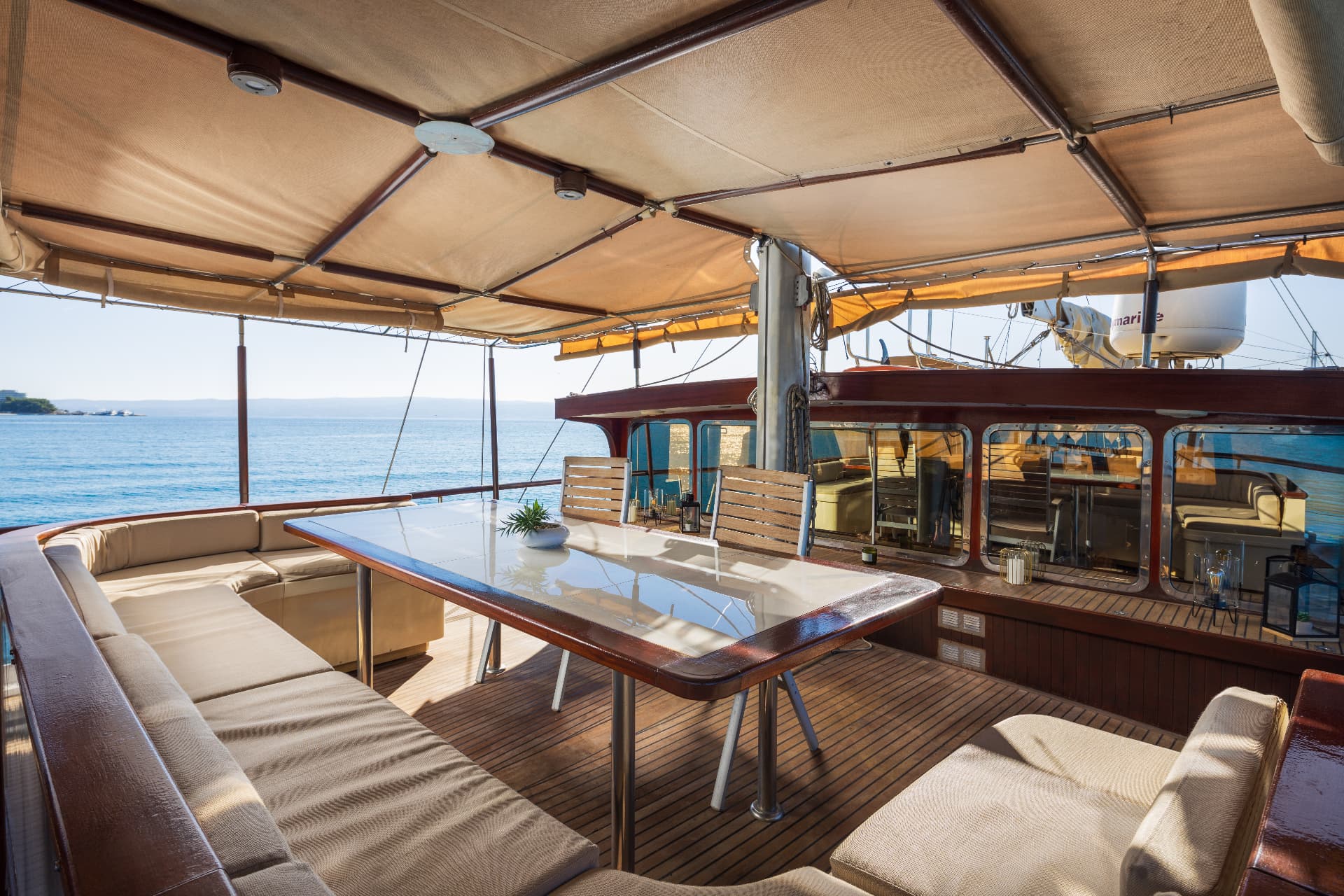 Outdoor dining area on boat deck with cushioned seating overlooking the blue sea.
