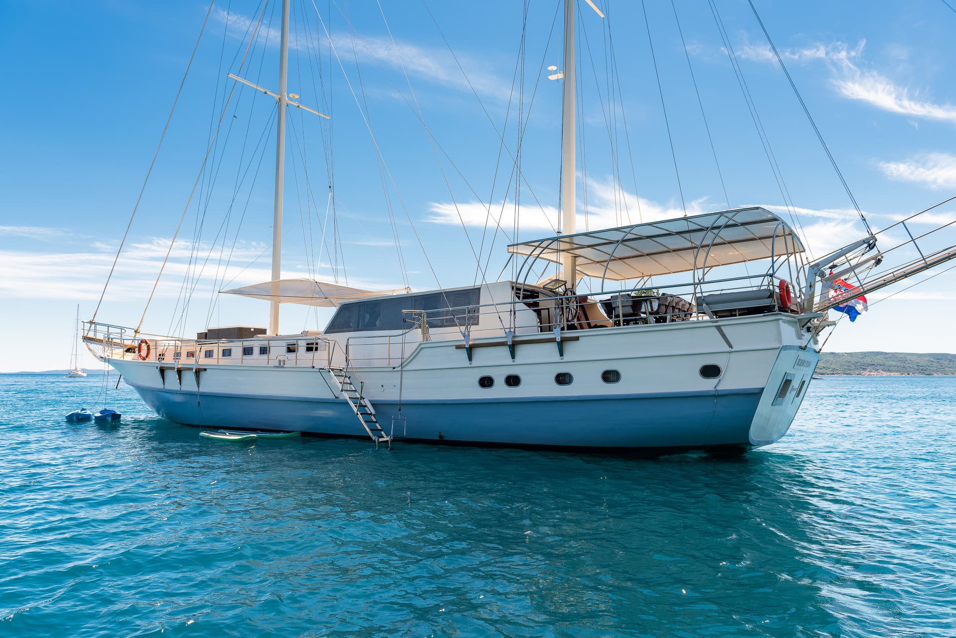 Large white and blue sailboat moored on turquoise water under a bright blue sky with clouds.