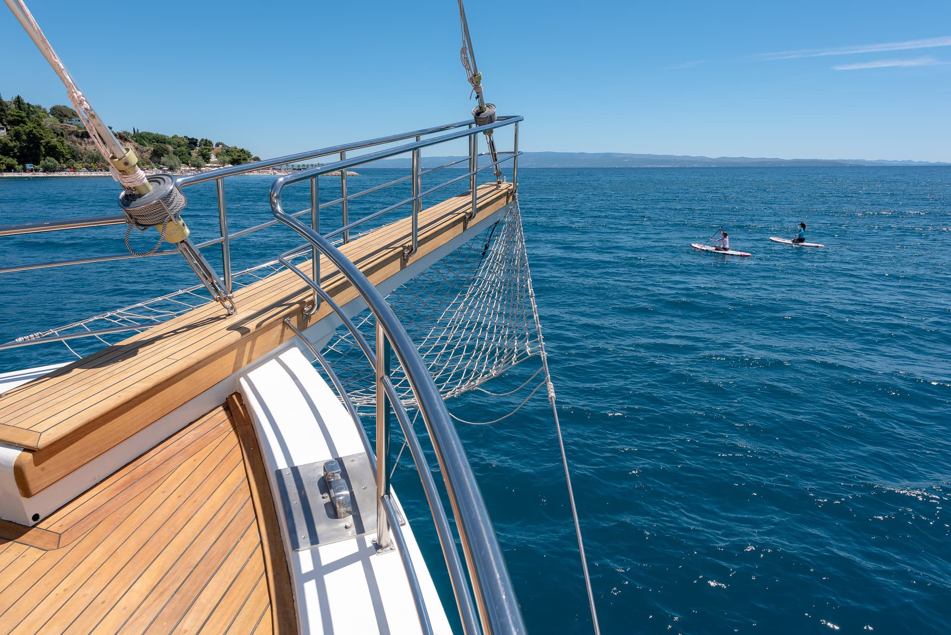 View from sailboat deck showing two people paddleboarding on deep blue coastal water.
