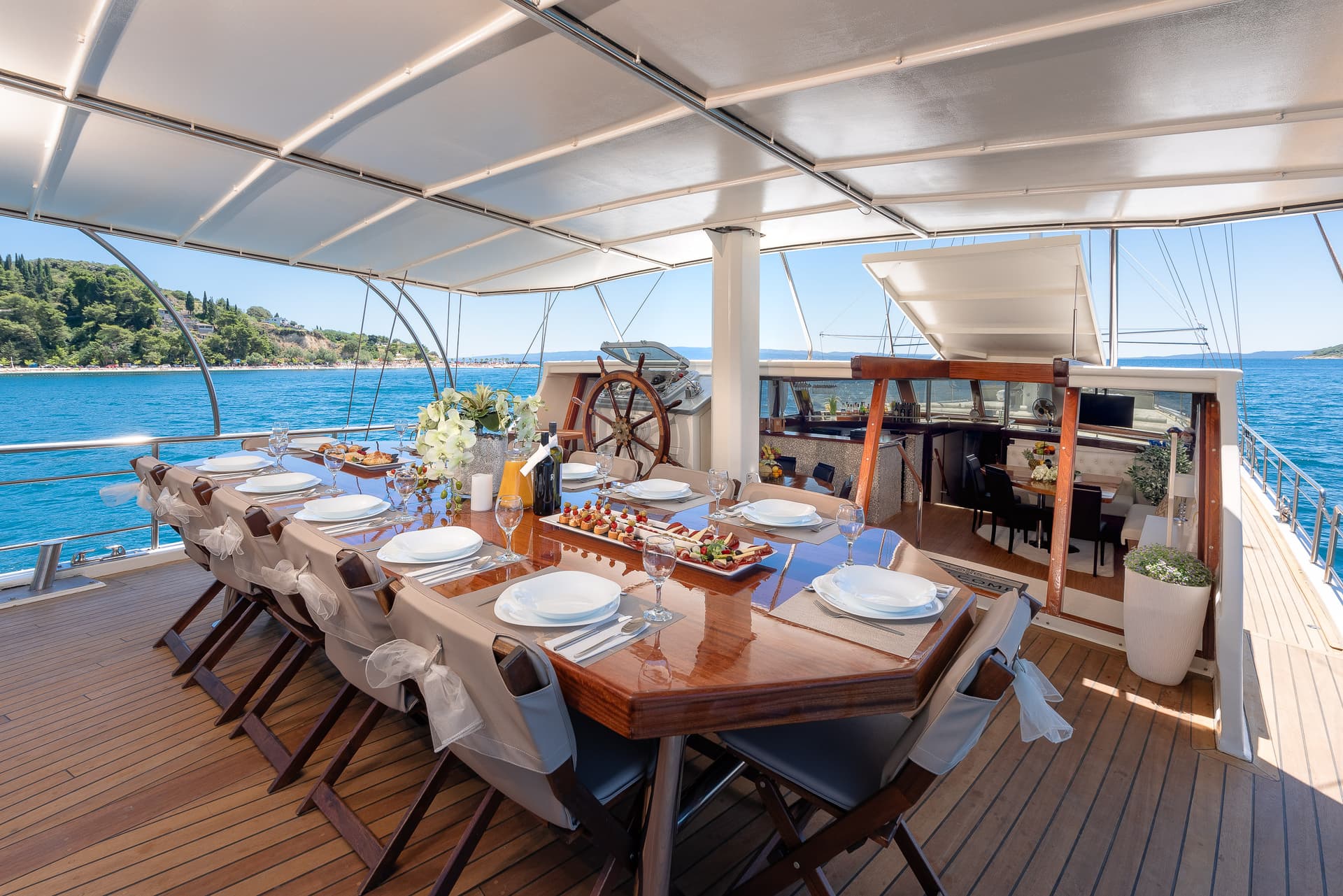 Dining table set for a meal on a boat deck near a lush, green coastline.