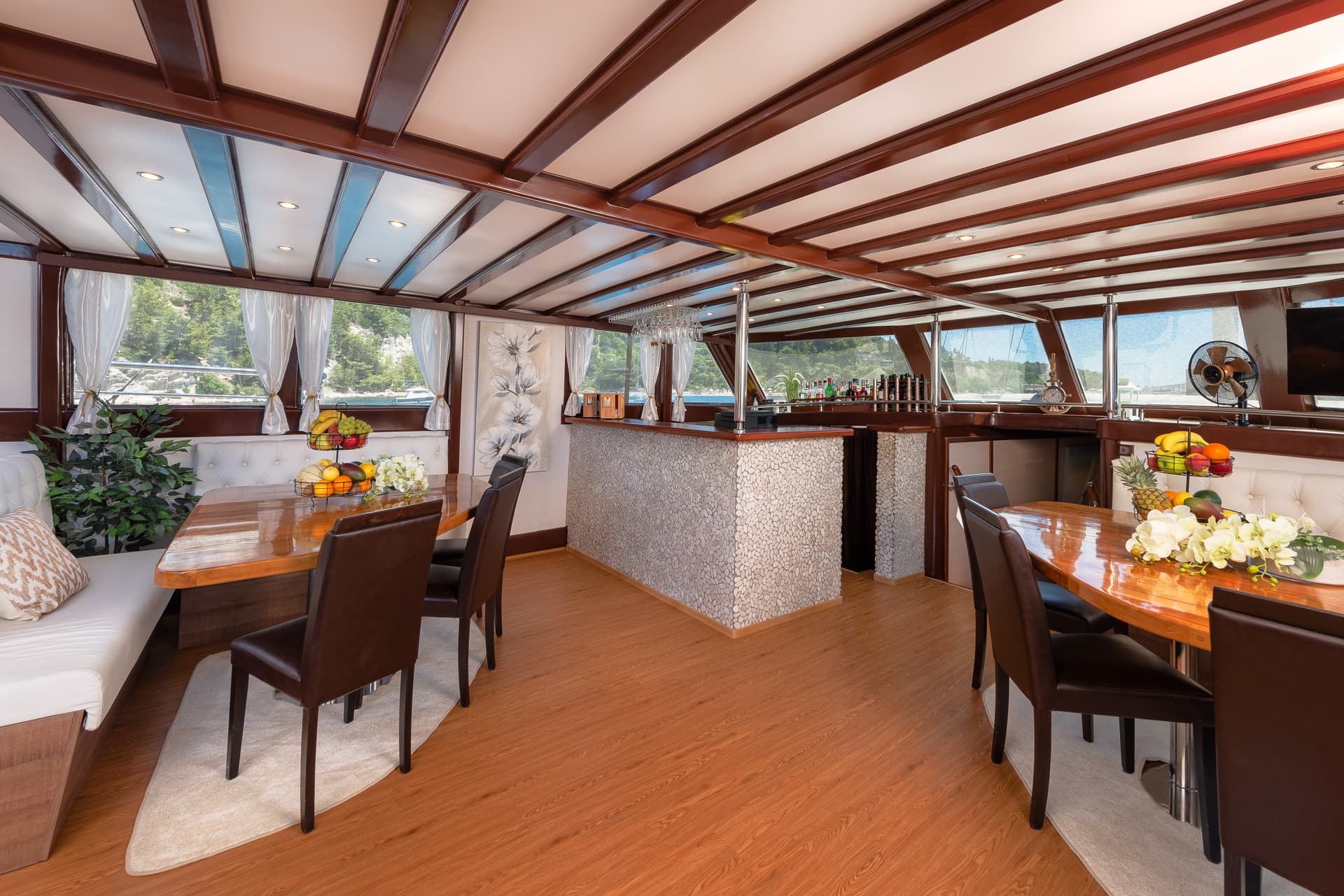 Interior dining area and bar on a boat with views of a tree-lined coast.