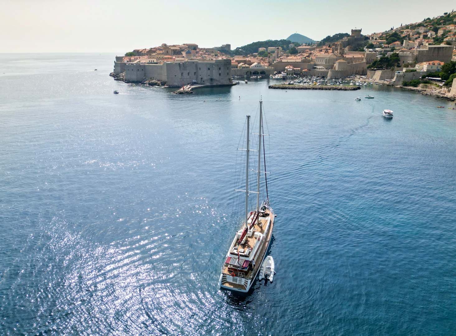 Large sailboat on blue water near historic walled city and harbor entrance