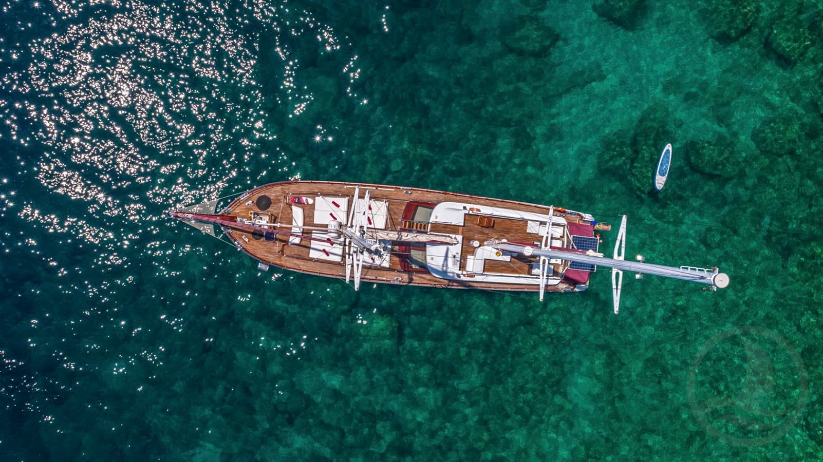 Aerial view of wooden sailboat anchored in clear turquoise water with sun glare