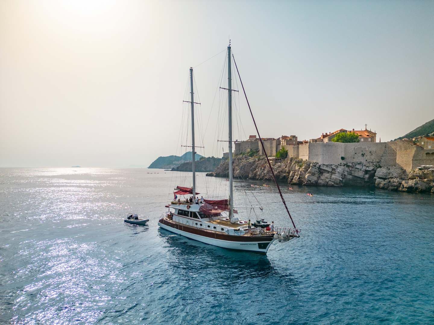 Large sailboat near historic stone city walls on sunny coastal waters