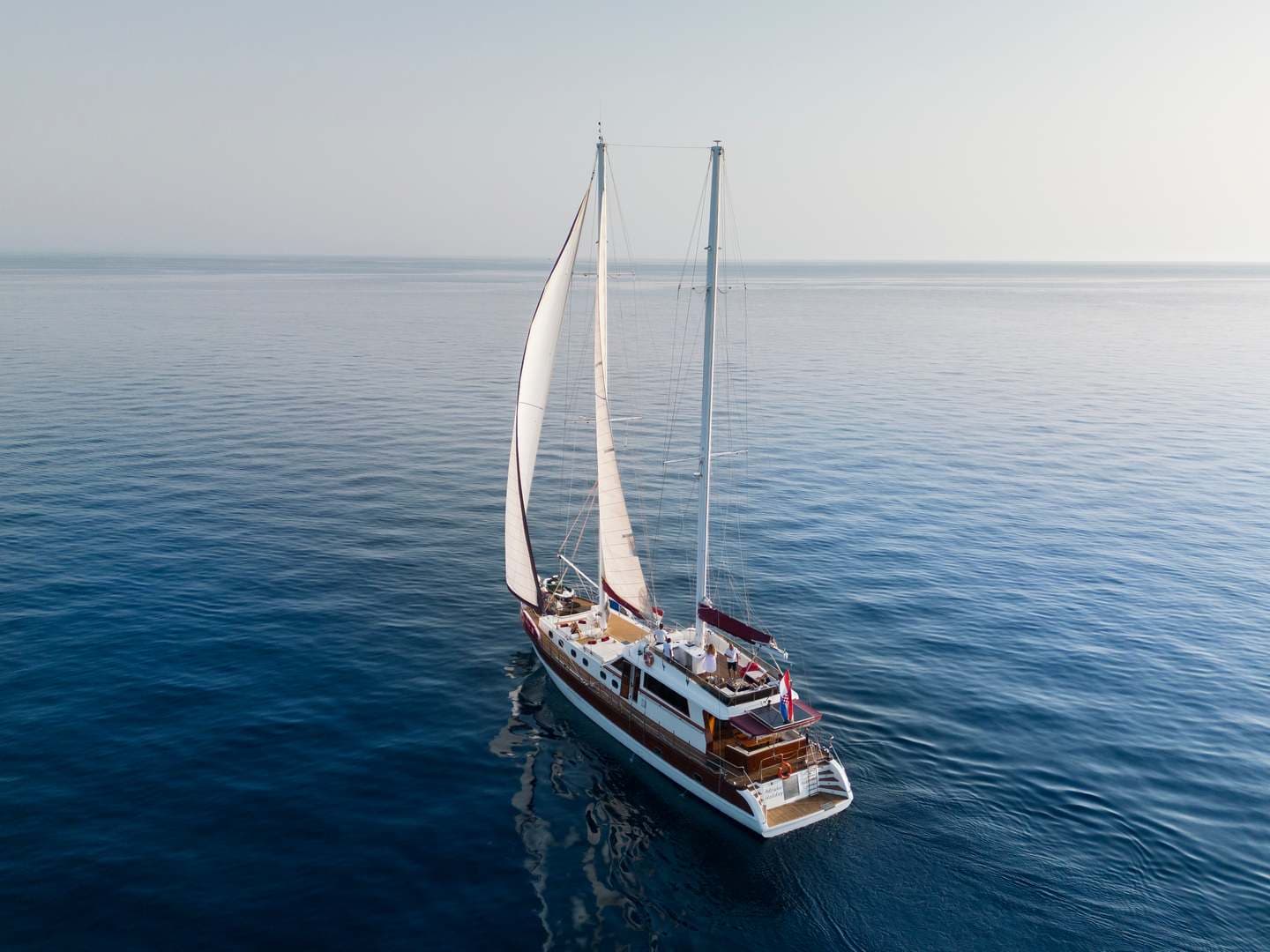 Two-masted sailboat with white sails cruising on deep blue, calm sea water