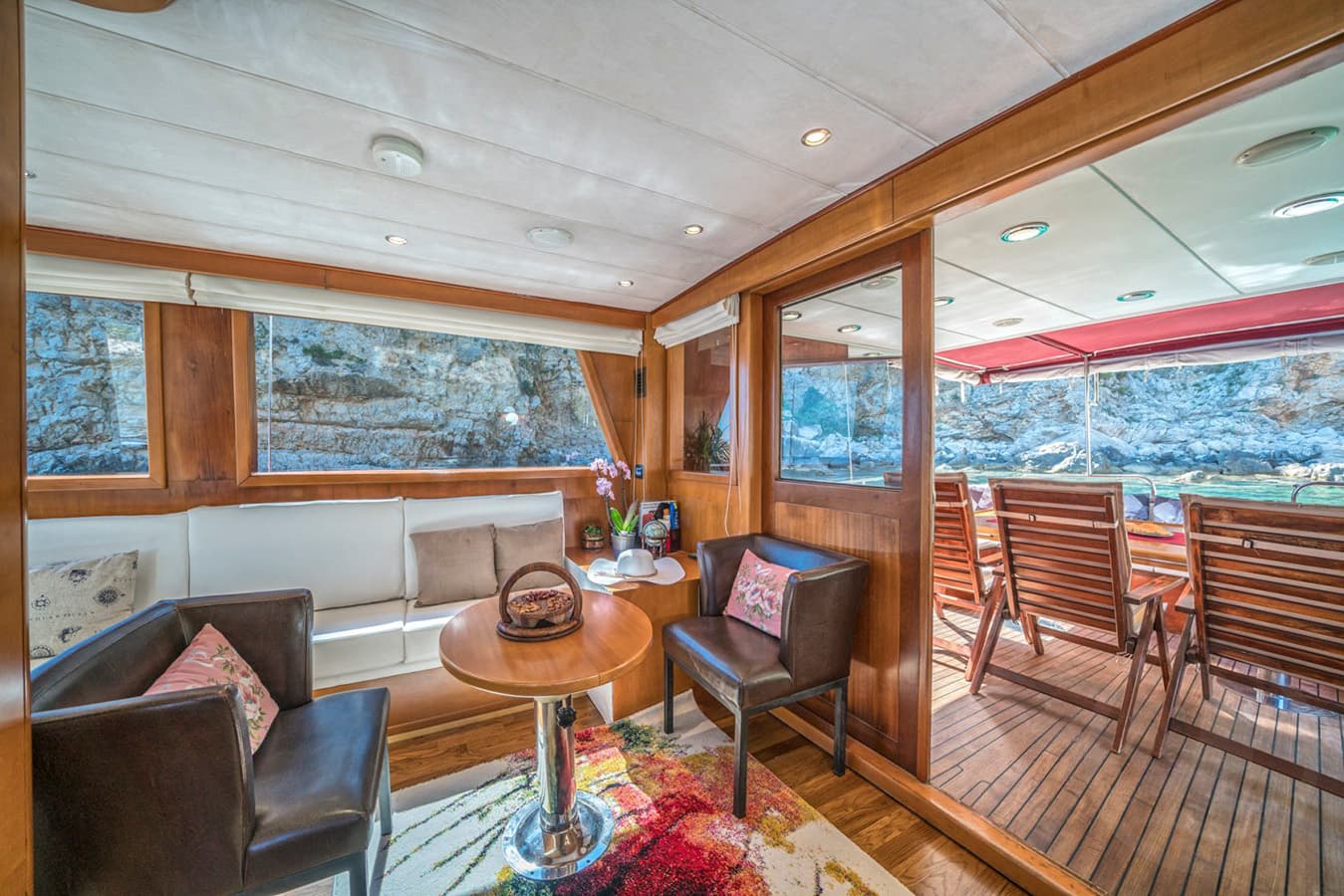 Boat interior lounge with wooden trim and view of rocky coastline outside