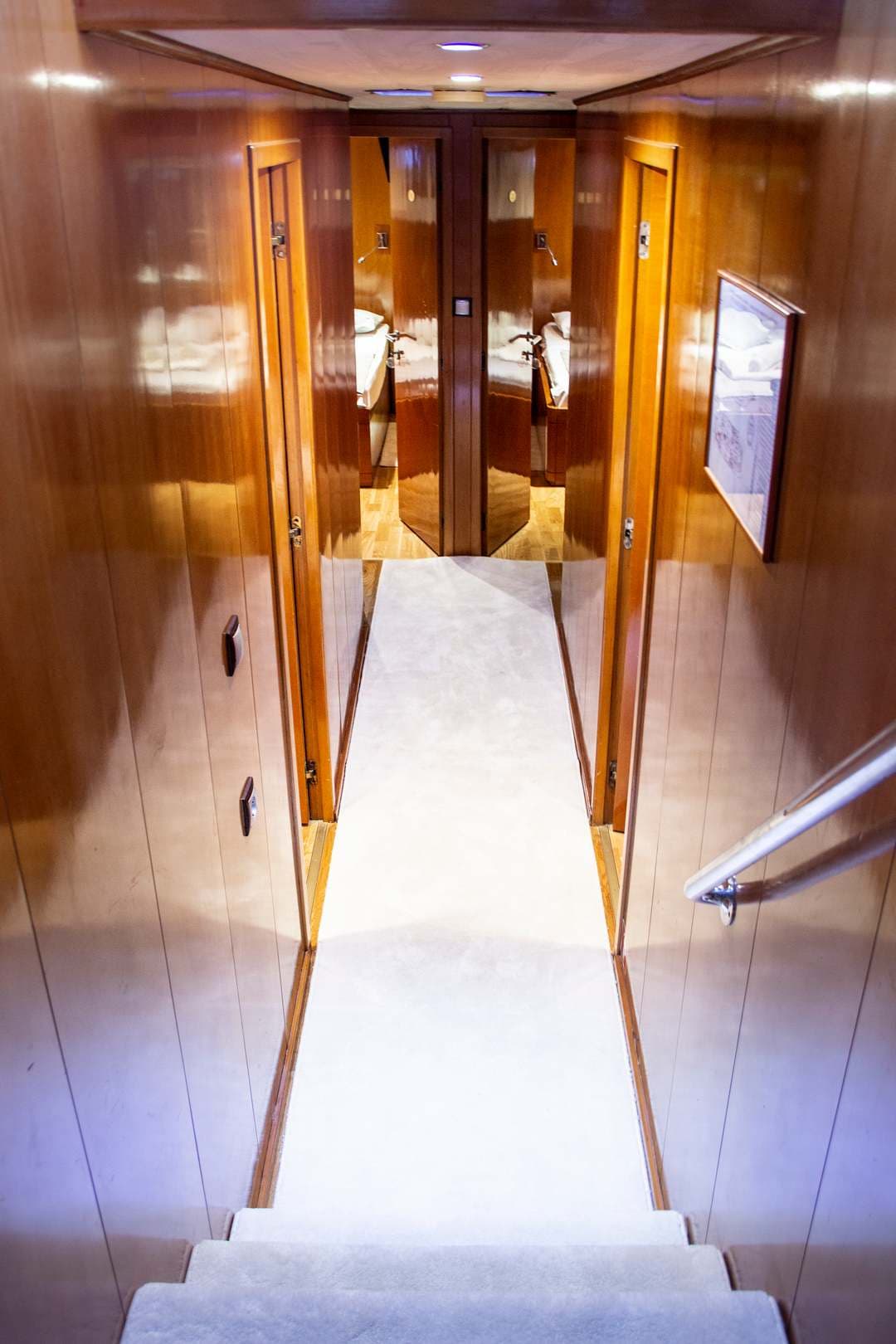 Stairway with white carpet leading to a hallway with wood paneling and cabin doors.