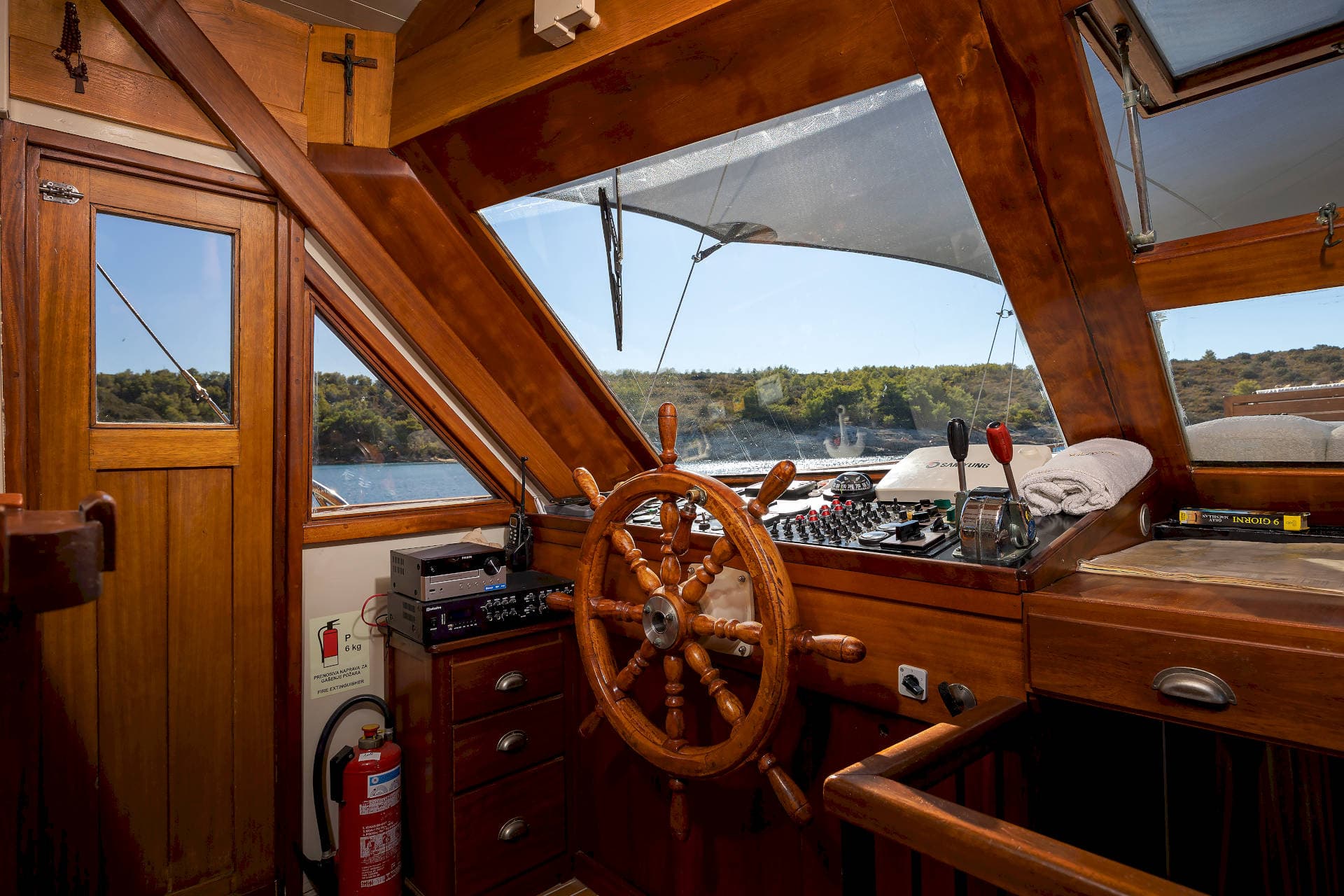 Wooden boat helm with controls, overlooking green coastline and blue water