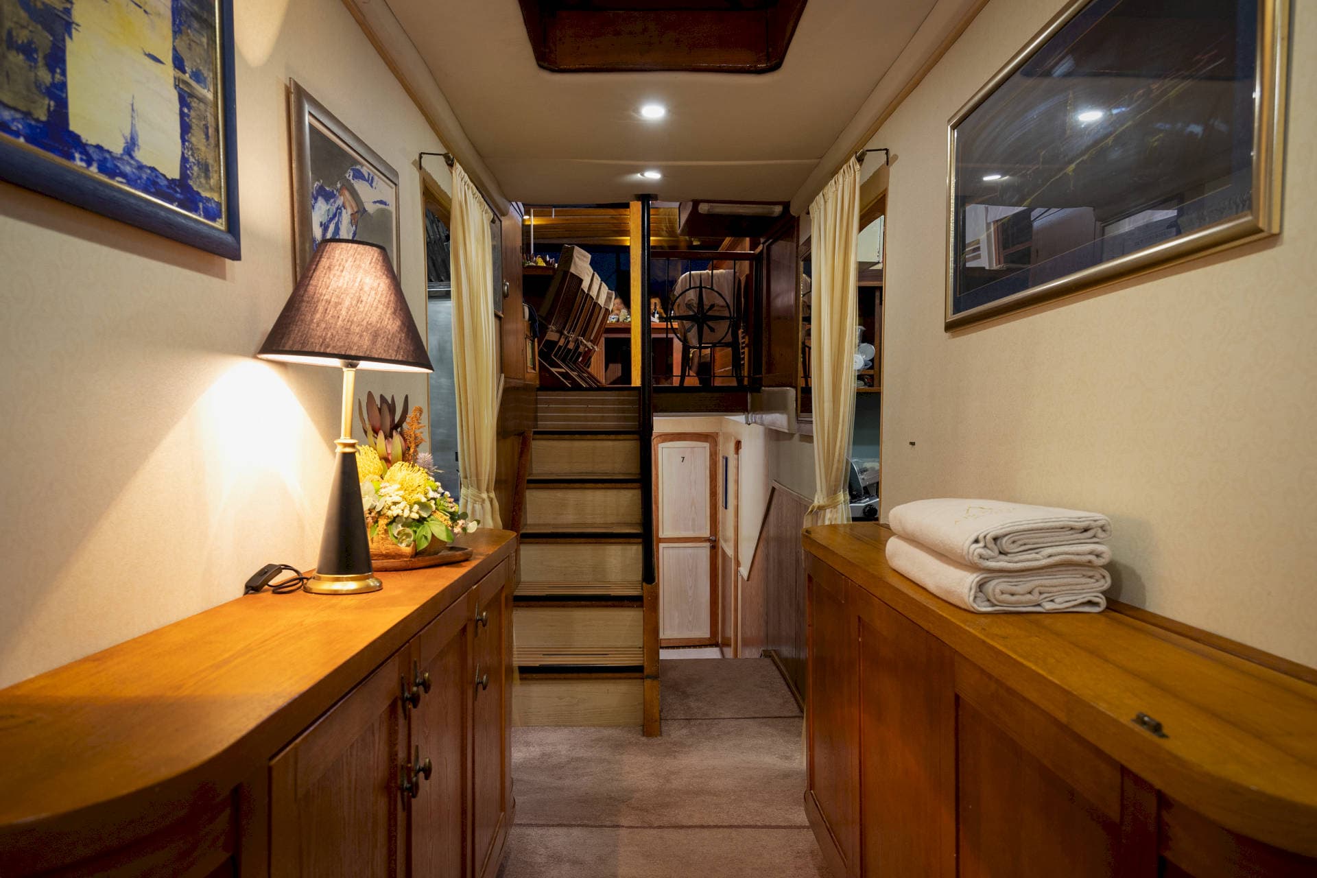 Interior hallway of a yacht with wood cabinetry, artwork, and stairs leading up to the helm.
