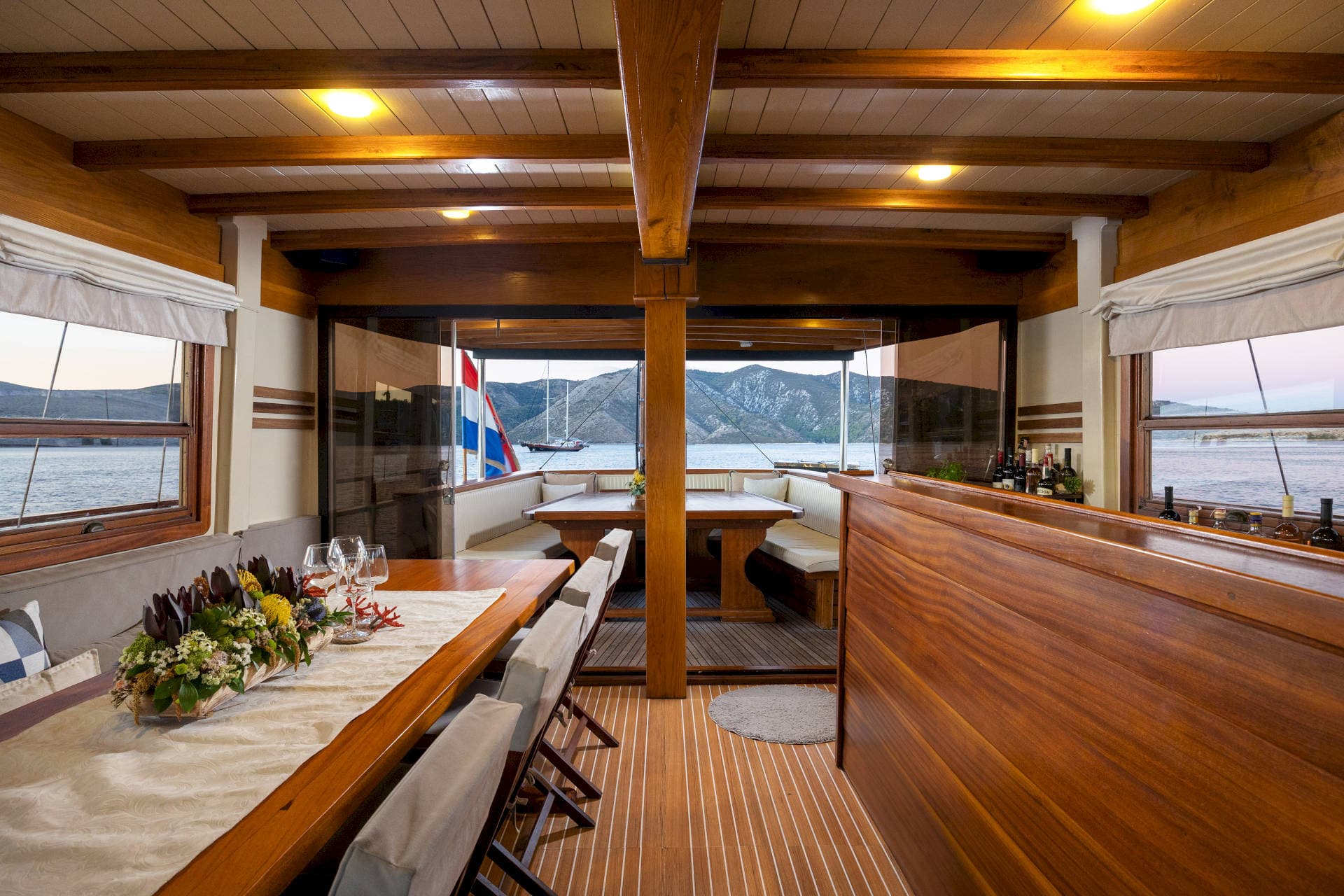 Interior dining area of a wooden boat with views of mountains and a Croatian flag.