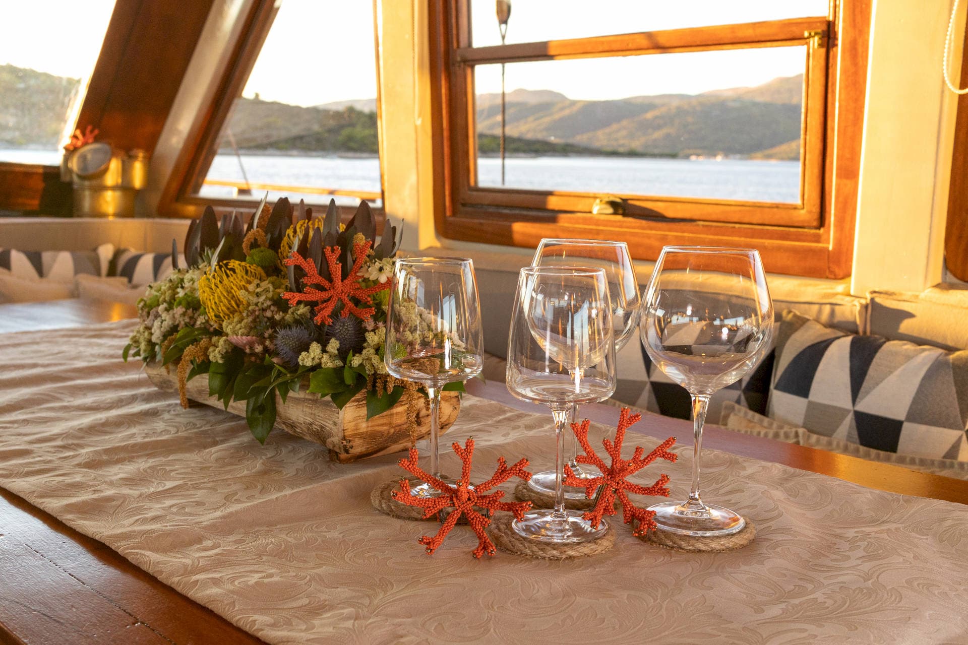 Wine glasses and floral centerpiece set on a table aboard a boat overlooking coastal mountains.