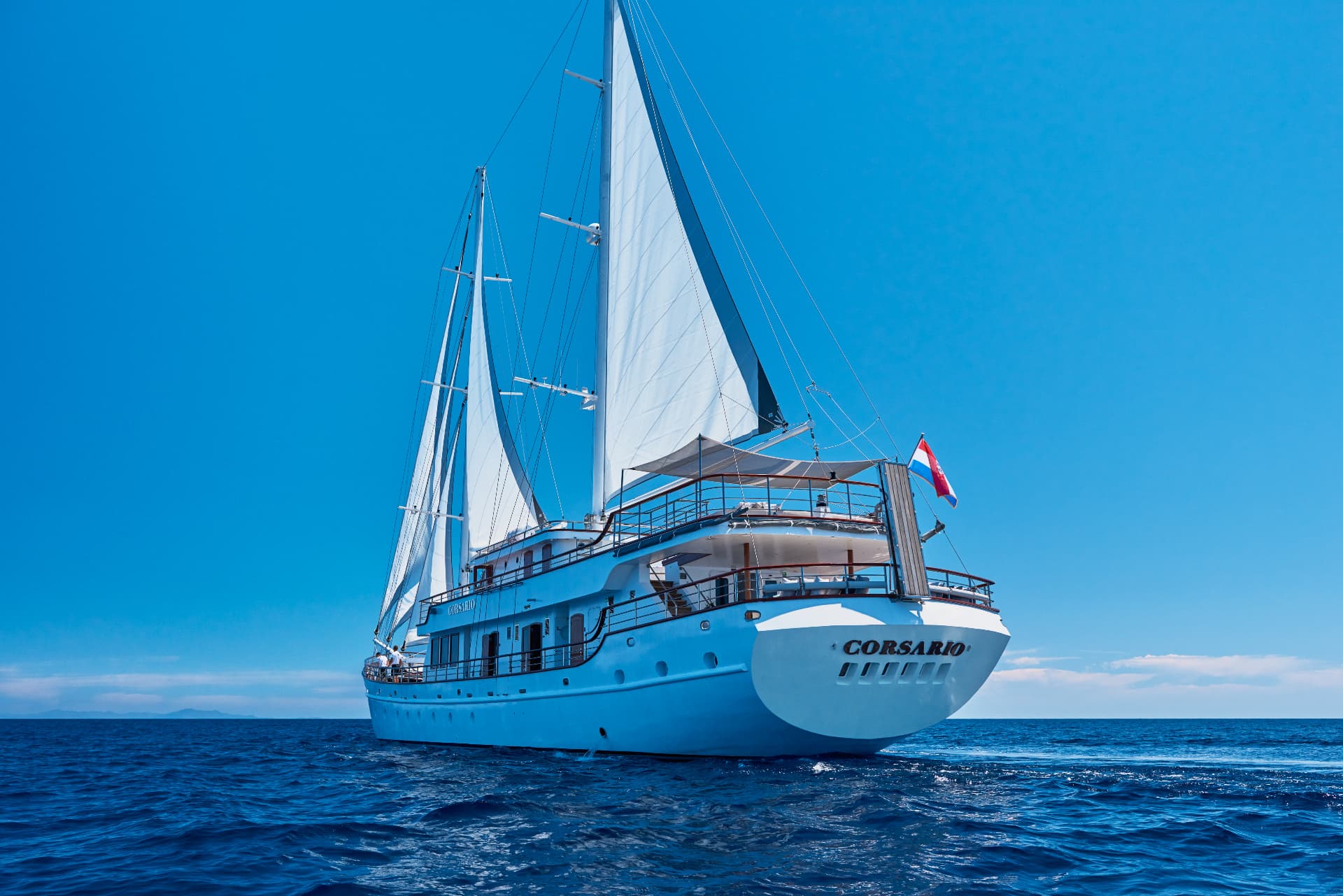White sailing yacht named Corsario on deep blue water under clear sky with distant islands.
