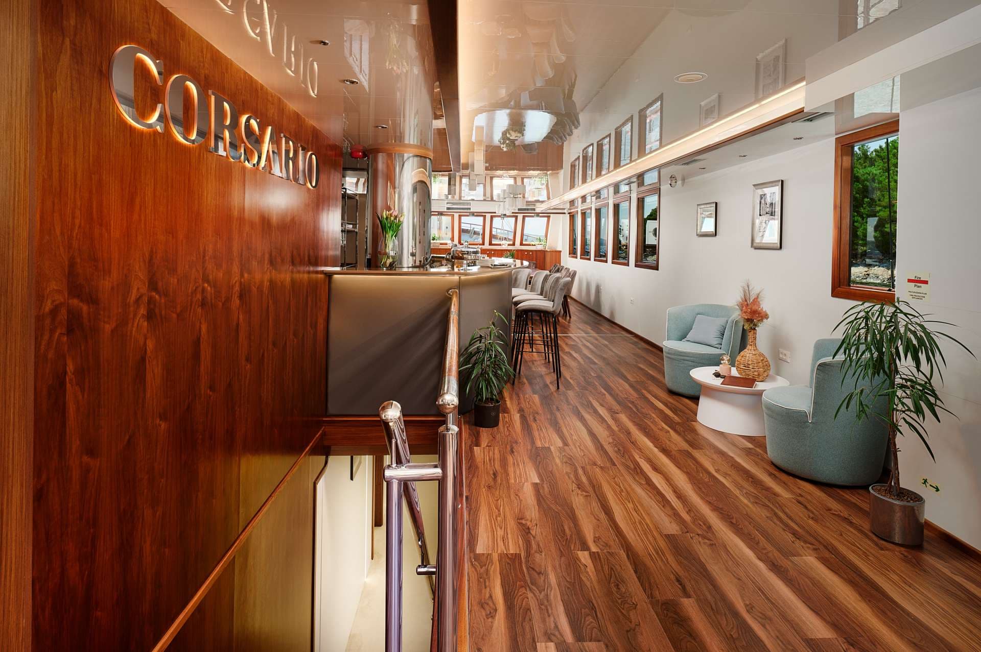 Interior lounge area with "CORSARIO" sign, bar, and seating on a boat or ship.