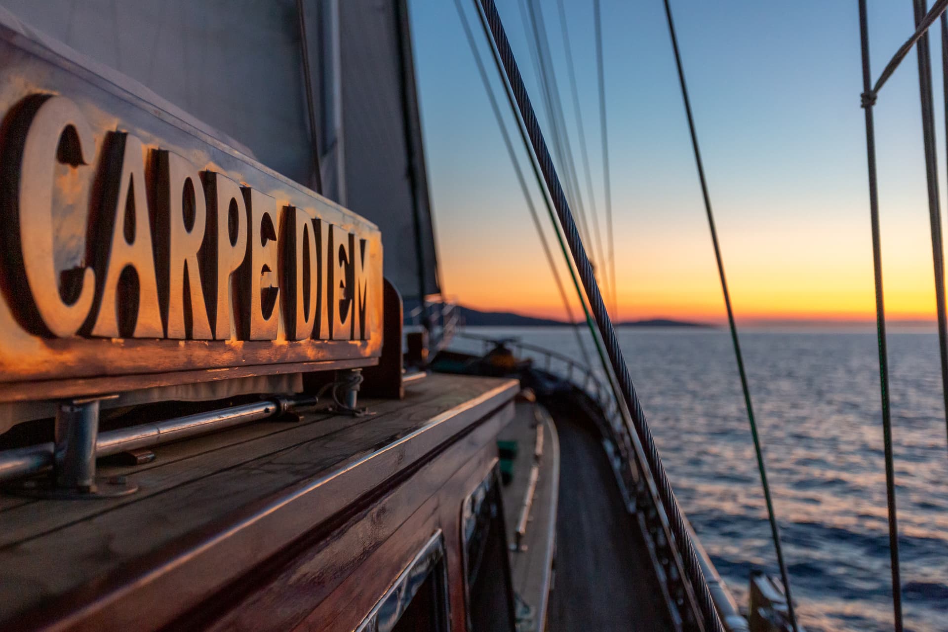 Wooden boat name "Carpe Diem" illuminated at sunset on the sea with mountain silhouette.