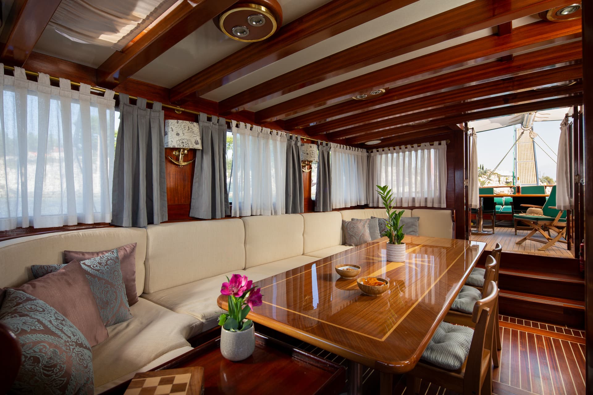 Interior salon of a wooden yacht with a glossy table, seating, and view to the deck.