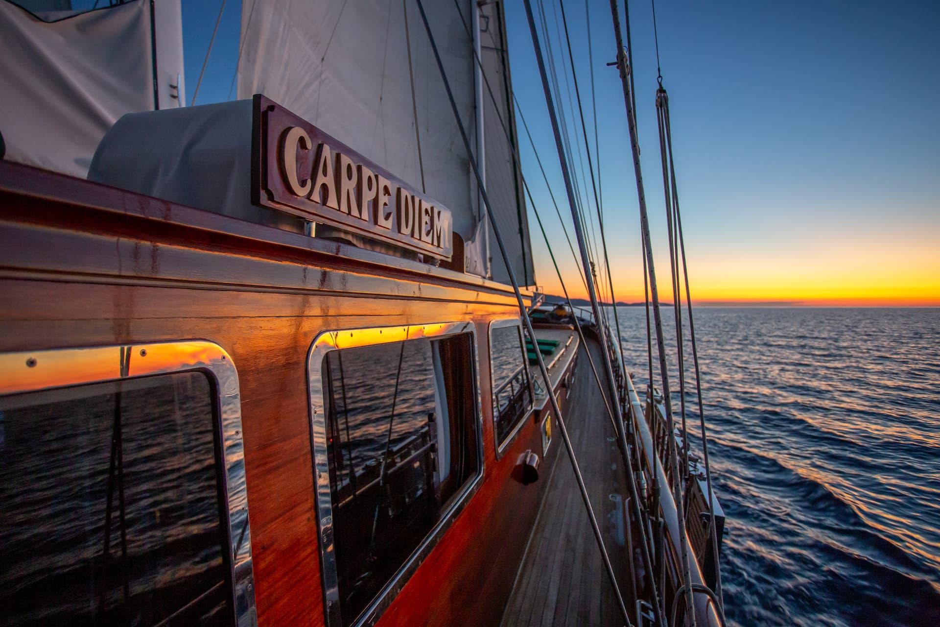 Sailboat deck with "Carpe Diem" sign sailing on the sea at sunset