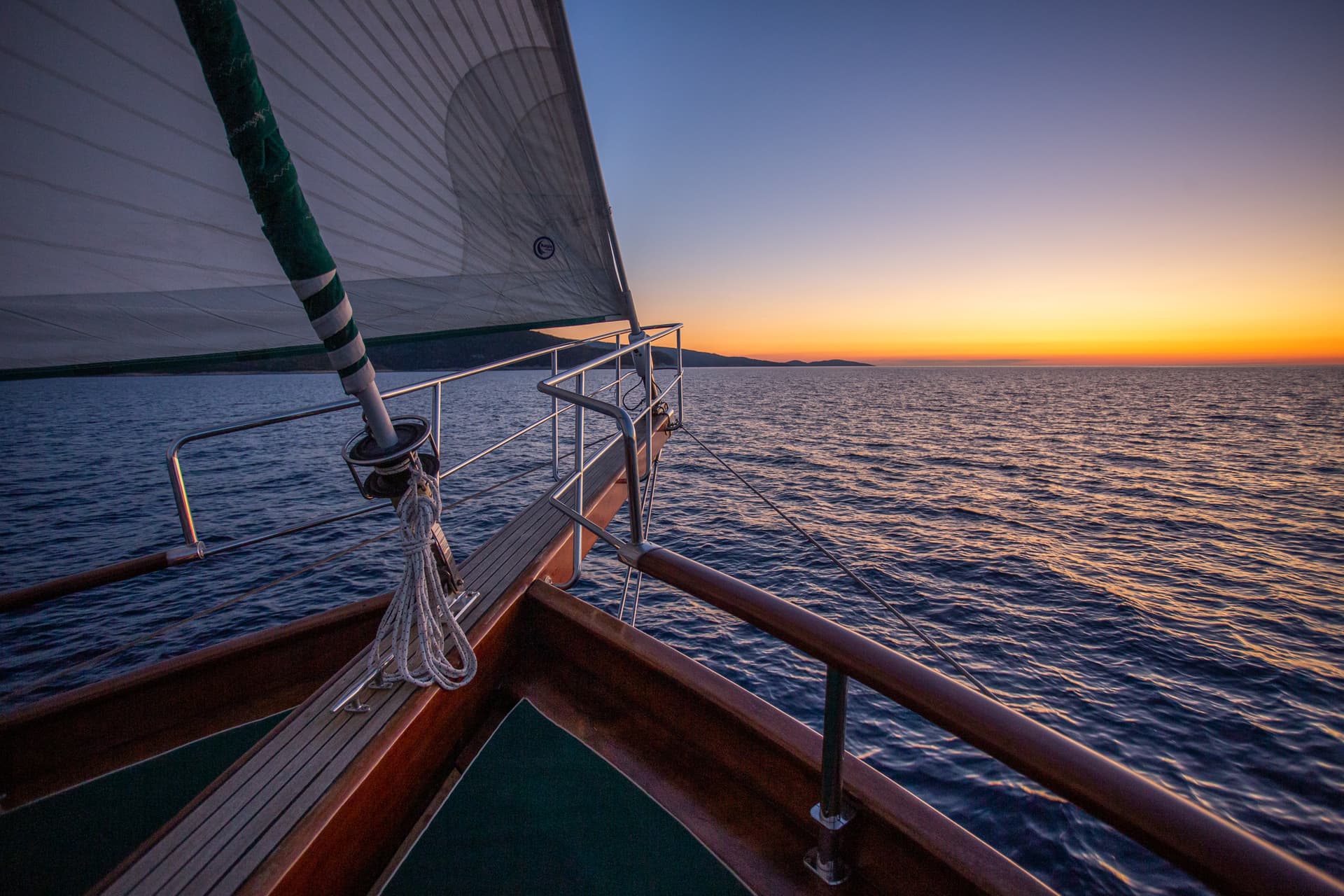 Sailboat bow on dark water with land silhouette at sunset