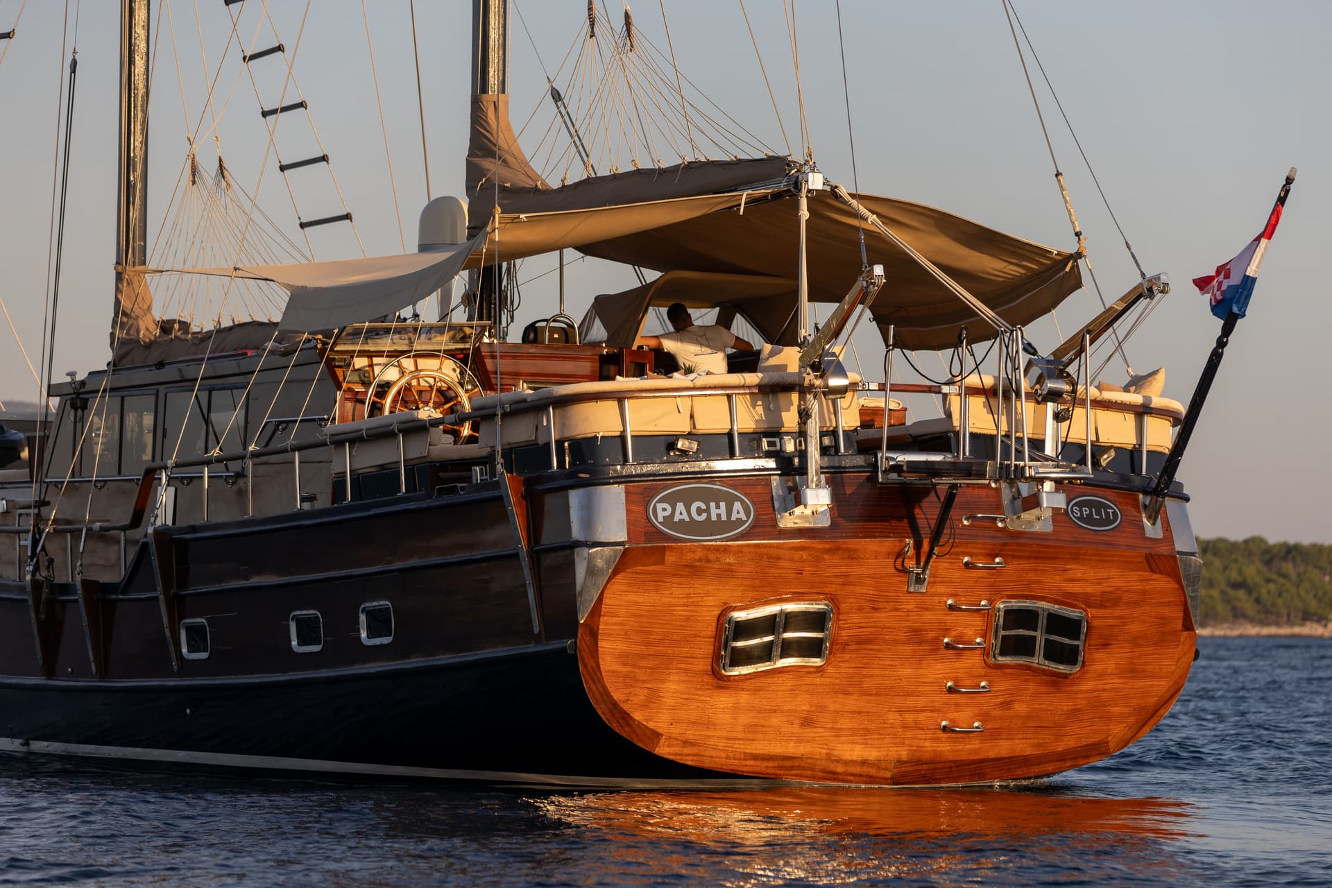Wooden yacht "Pacha" from Split sailing on dark blue water near a wooded coastline.