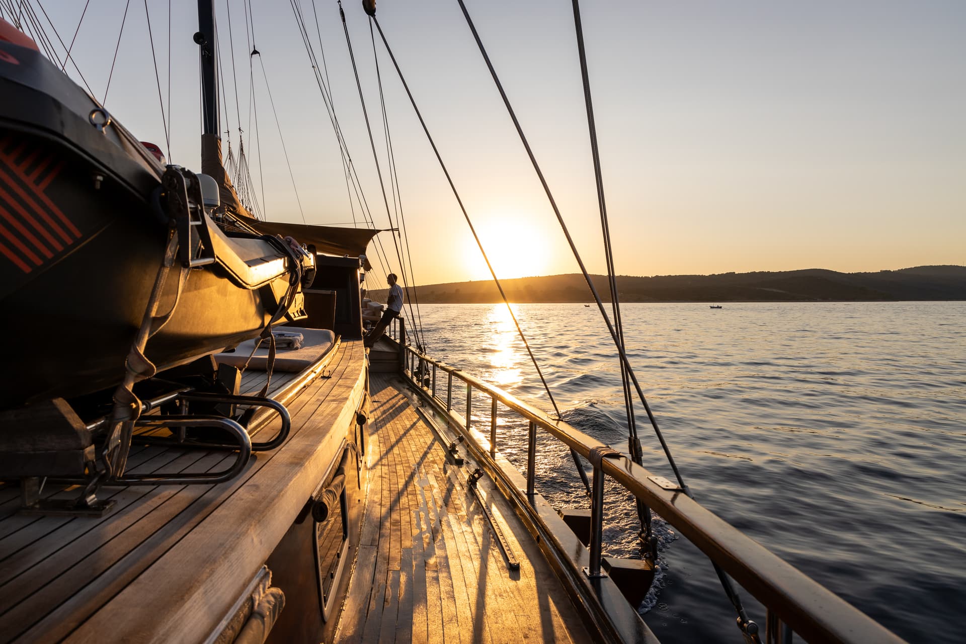 View from sailboat deck toward sunset over hilly coastline and calm water