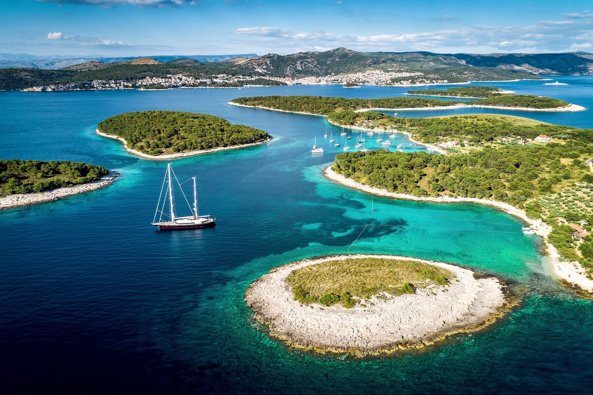 Large sailboat on deep blue water near green Croatian islands and distant coastal town.