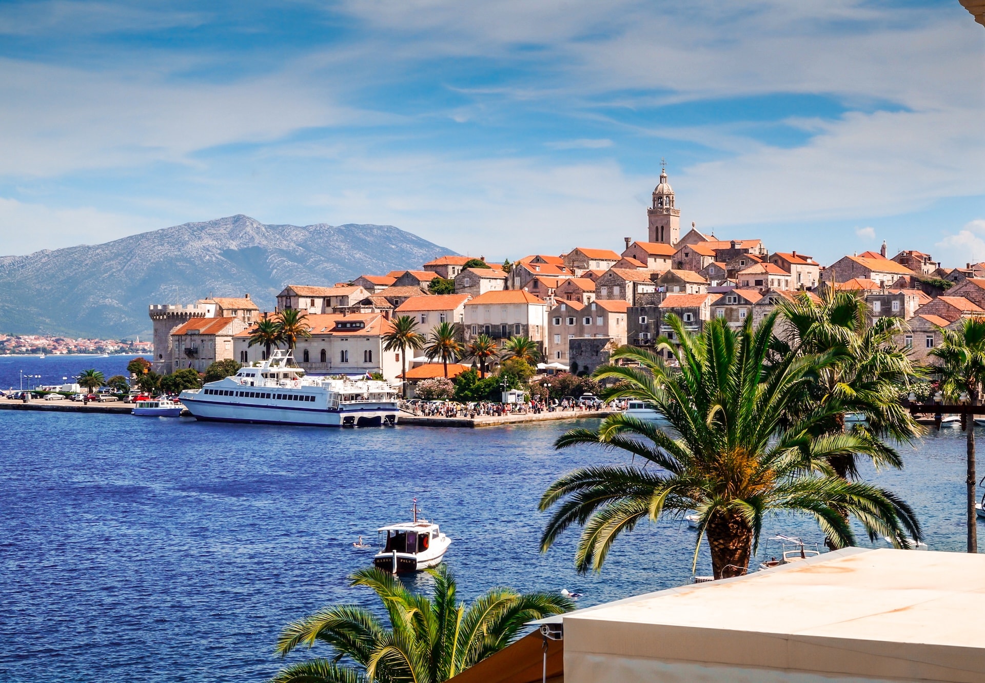 Yacht and small boat on blue water near Korcula Island town with terracotta roofs and mountains.
