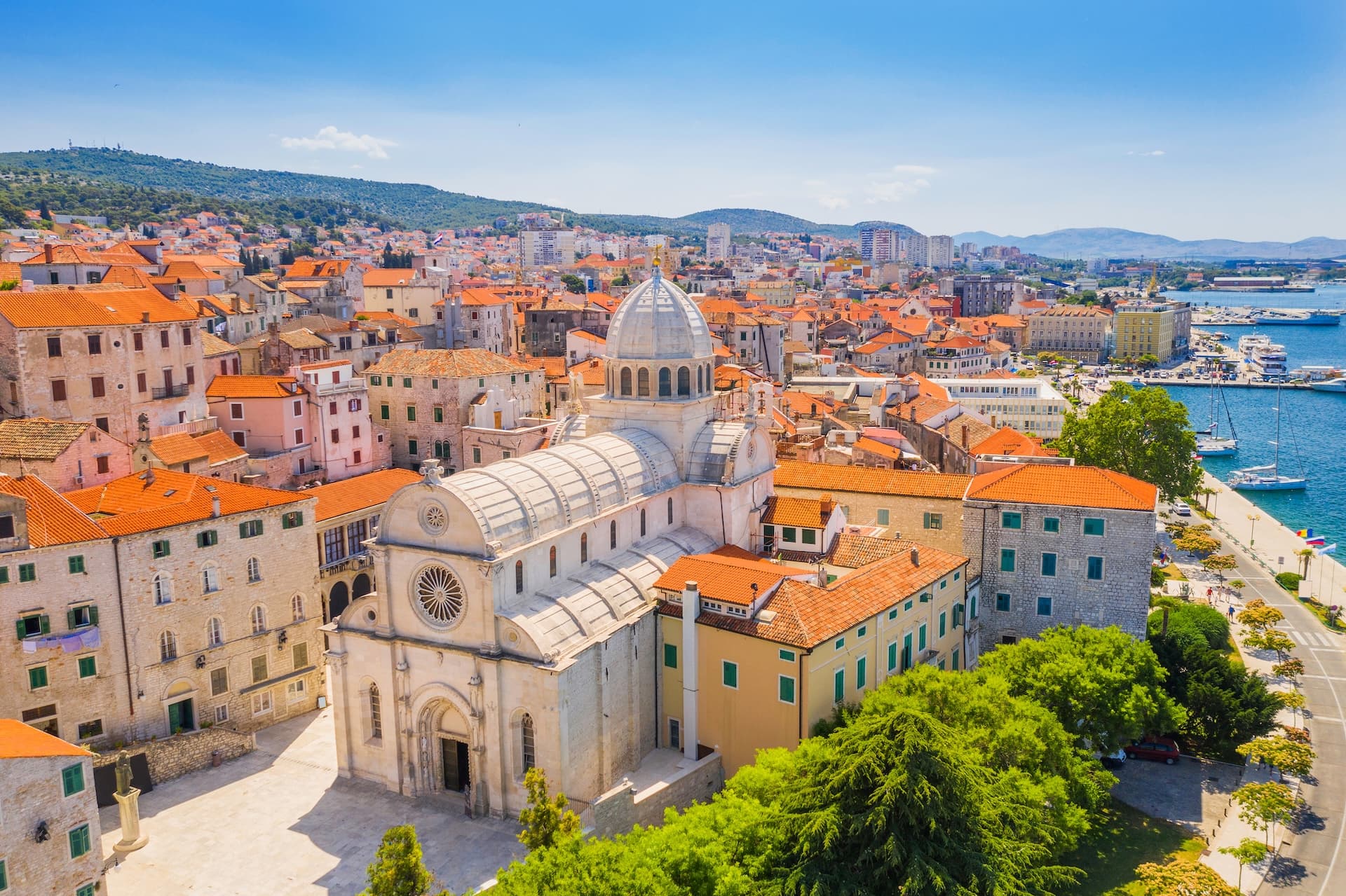 St Nicholas Cathedral in Sibenik with orange tiled roofs and blue Adriatic Sea harbor.
