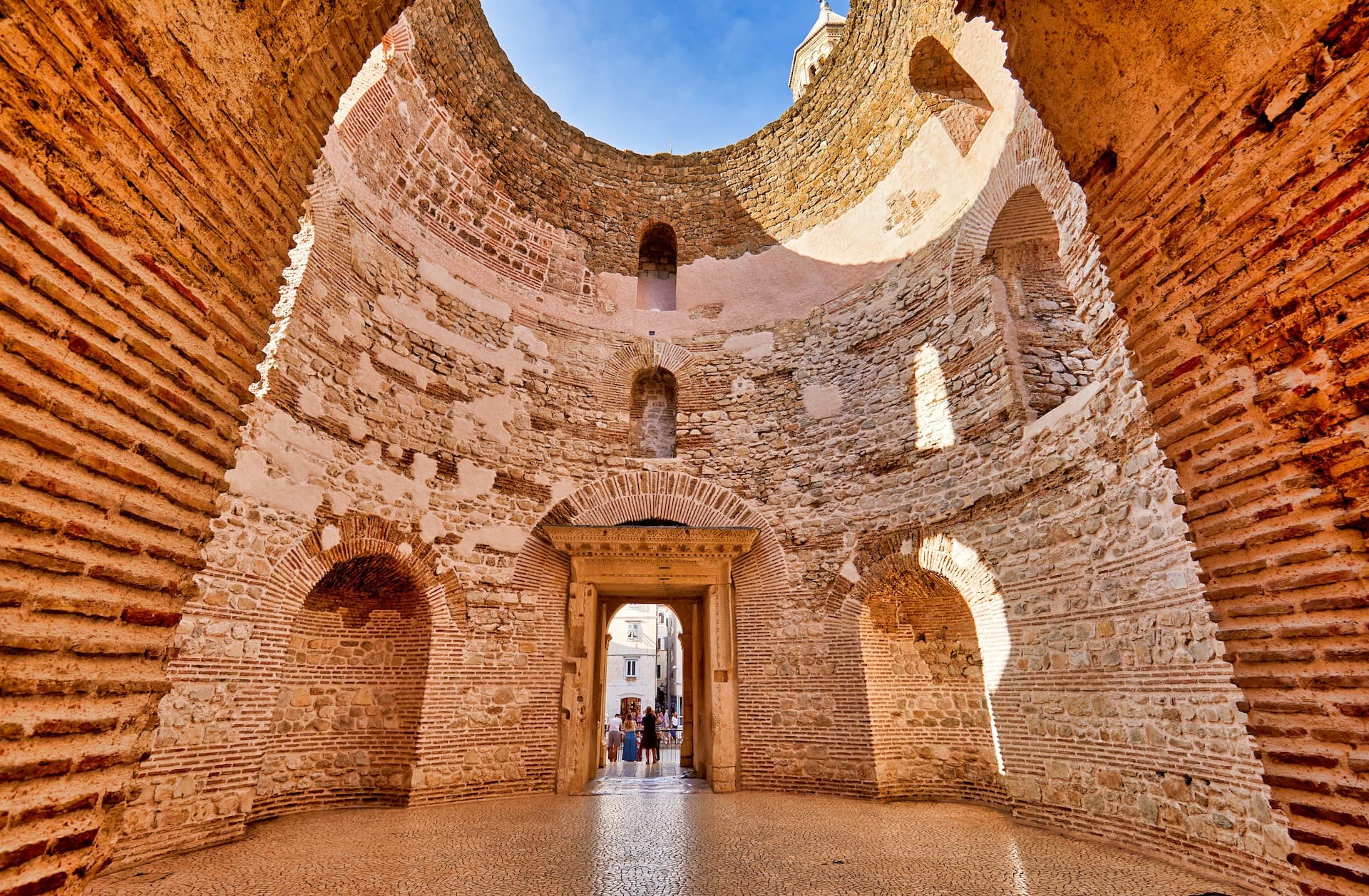 Interior of ancient stone structure with arched doorways opening to a sunny street in Split, Croatia.