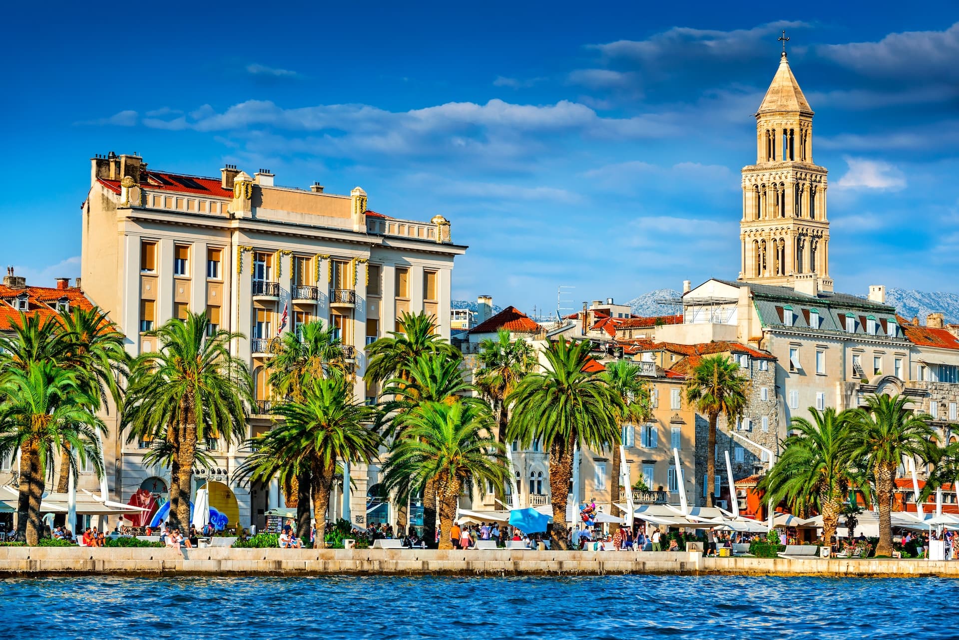 Waterfront promenade with palm trees, bell tower, and buildings in Split, Croatia.
