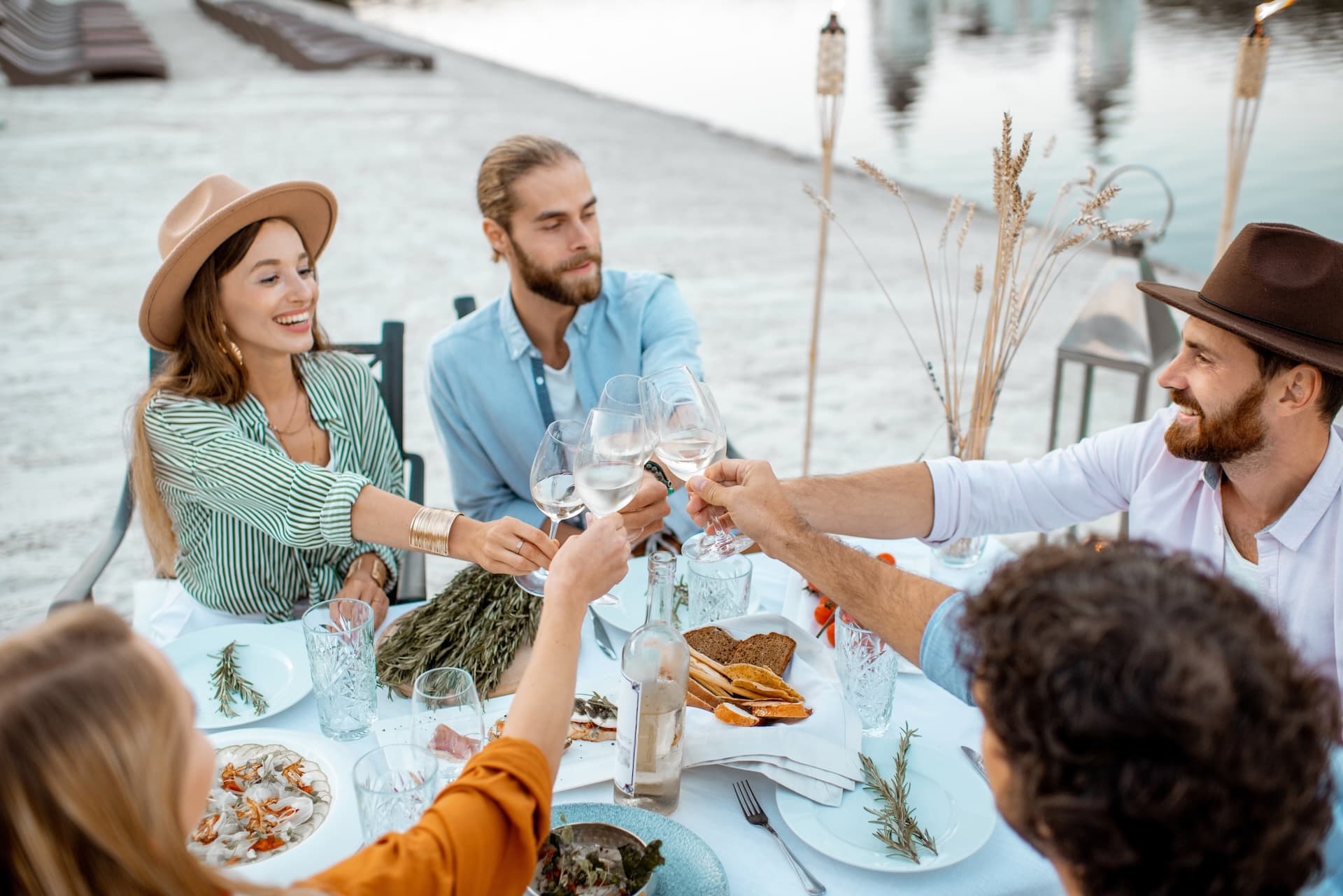 Friends toasting with white wine glasses during outdoor dinner near water in Korčula.