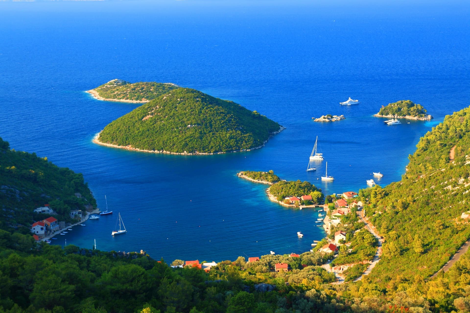 Yachts and boats in blue water near green islands and coastal village on Mljet Island.