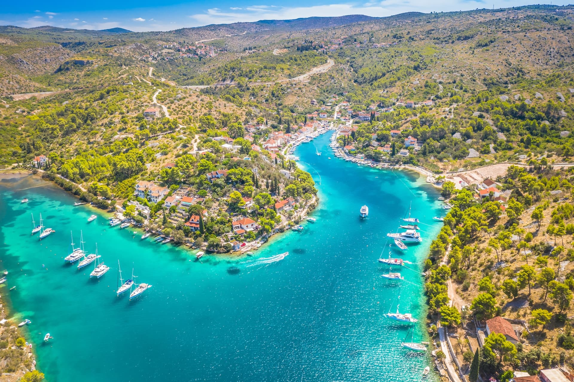 Boats anchored in turquoise bay next to a coastal village nestled in green hills