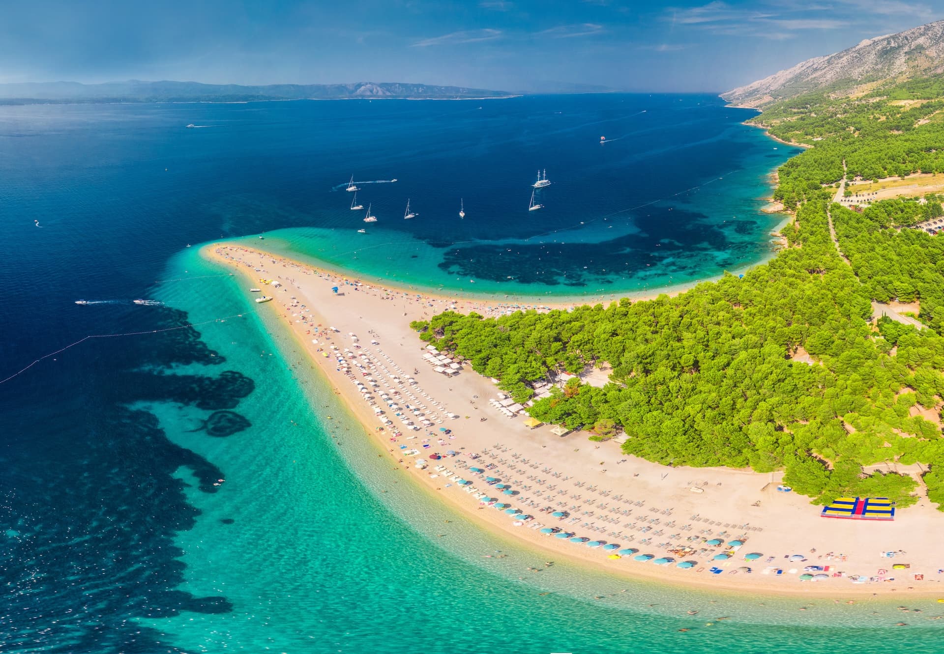 Aerial view of Zlatni Rat beach, a white pebble spit with turquoise water and sailboats.