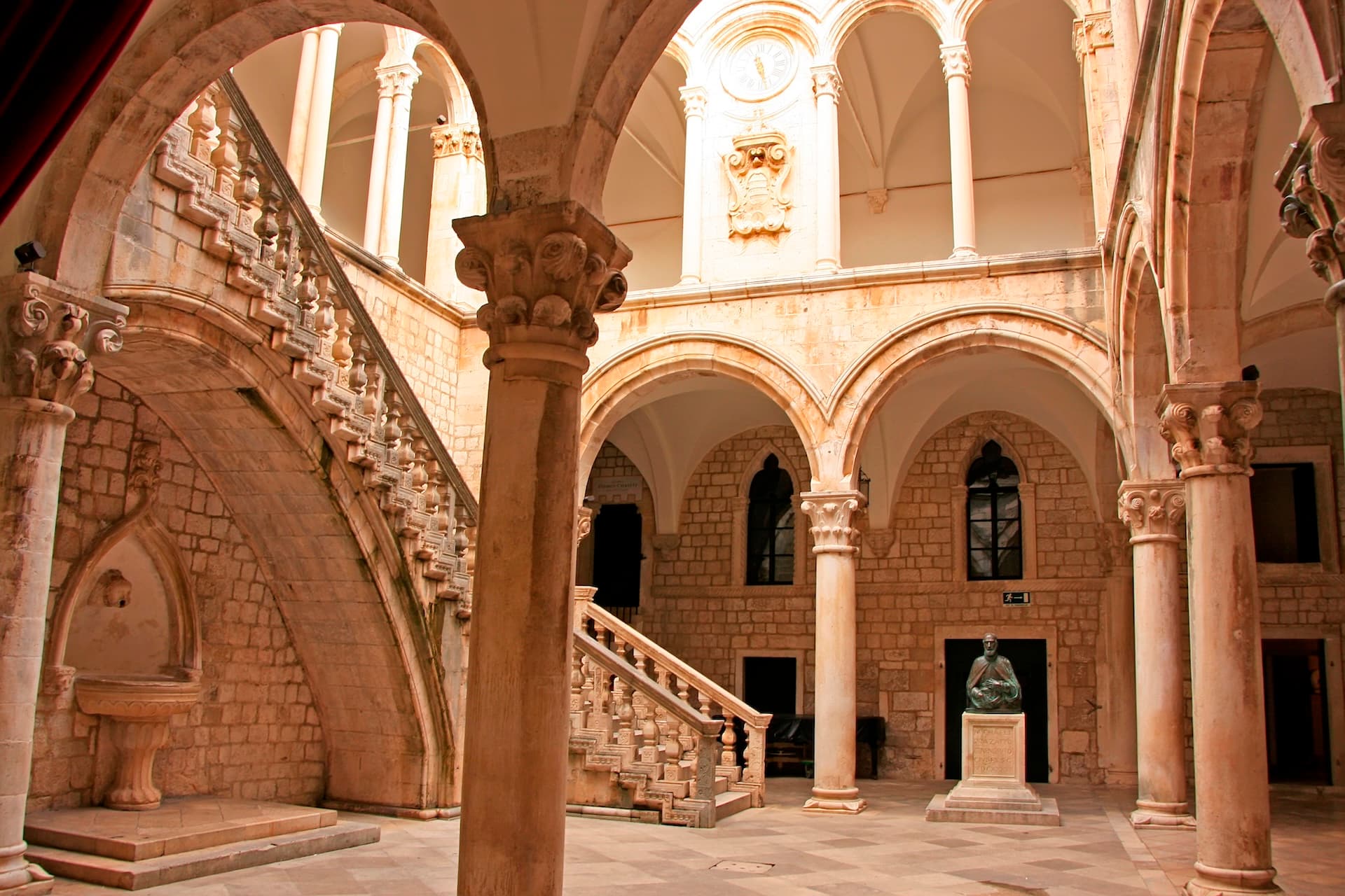 Stone courtyard with arched loggia, grand staircase, and statue in Dubrovnik heritage building.