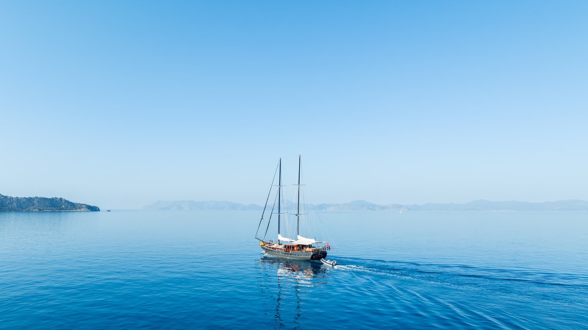 Gulet sailboat with masts moving across calm blue Adriatic Sea near coastline