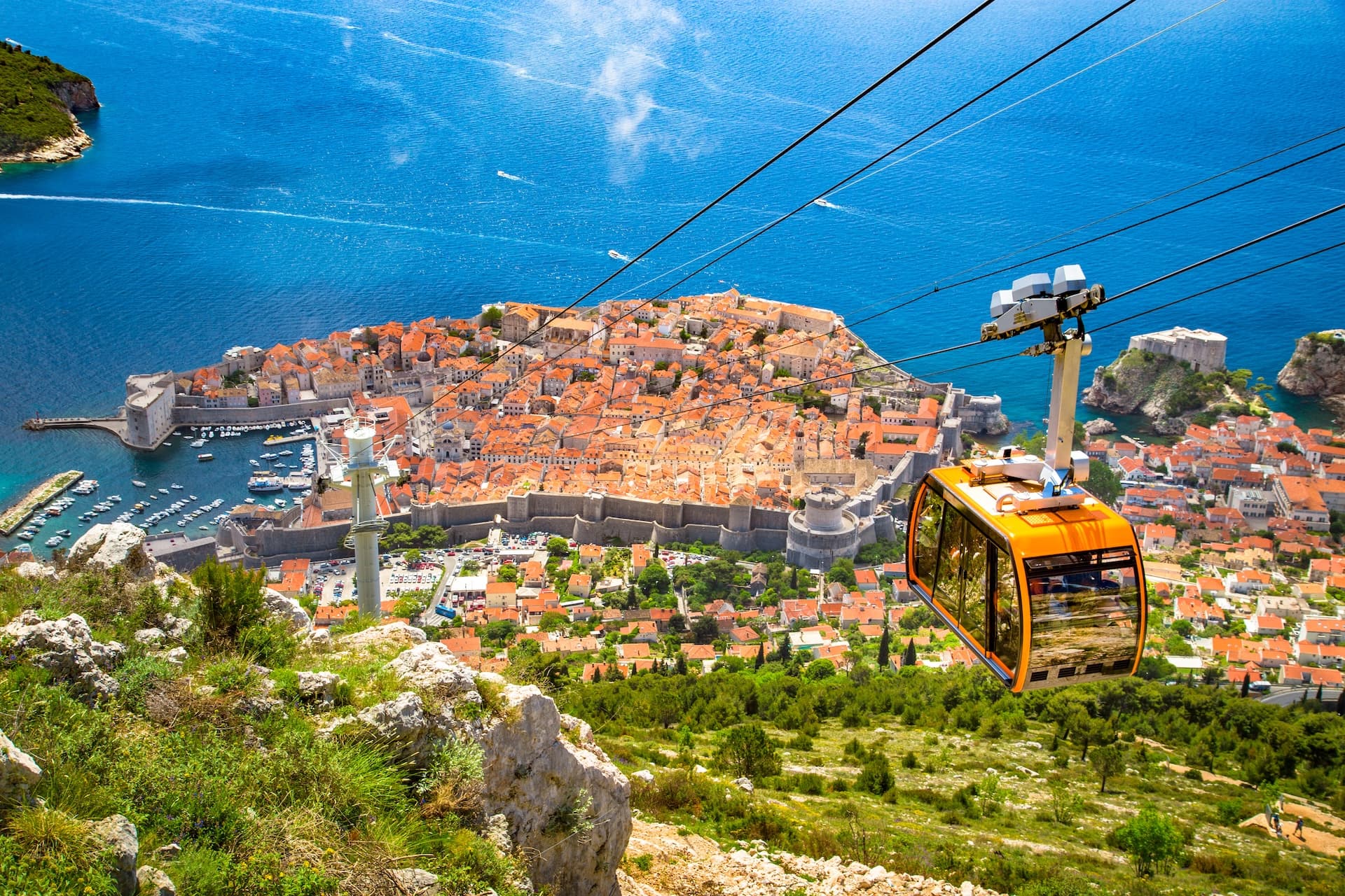 Dubrovnik cable car ascending over walled old town and blue Adriatic Sea.