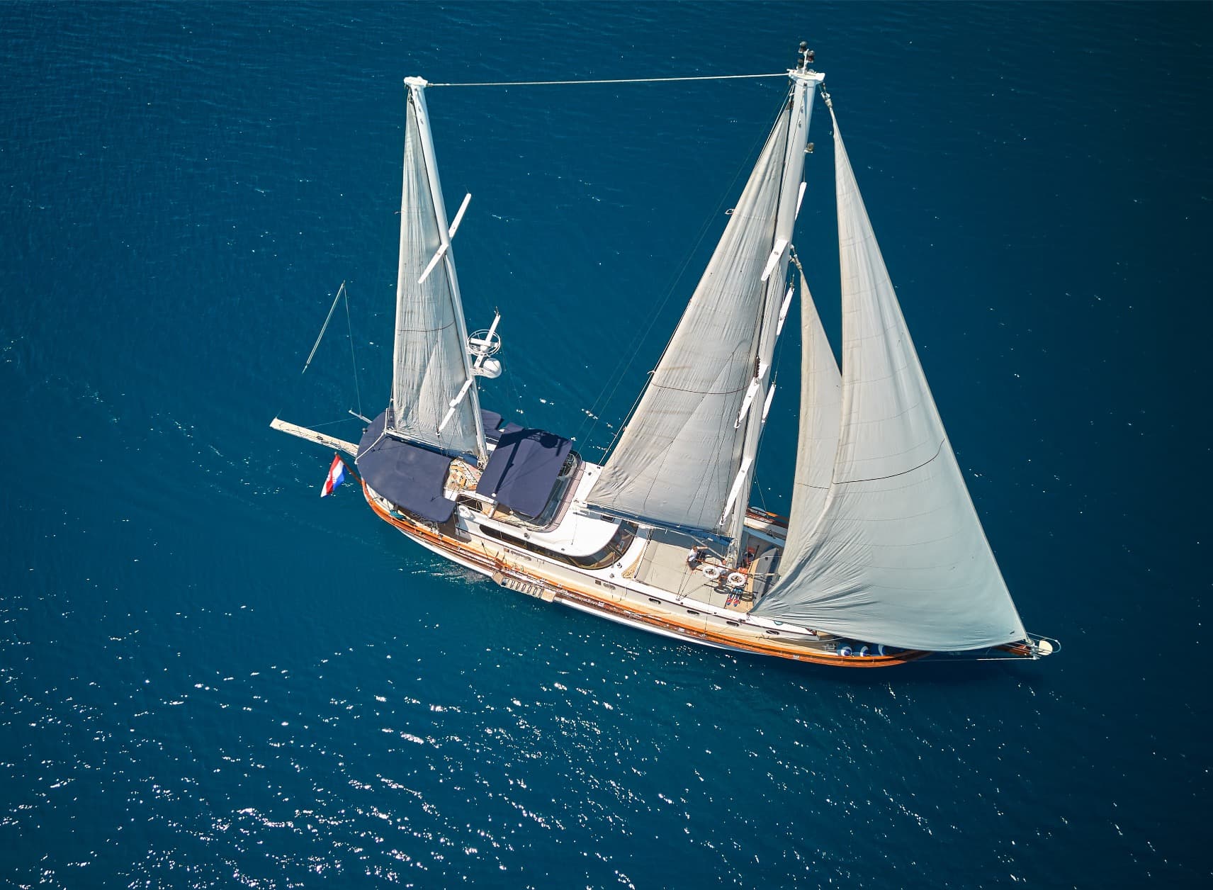 Sailboat with white sails on deep blue, sparkling sea water, aerial view